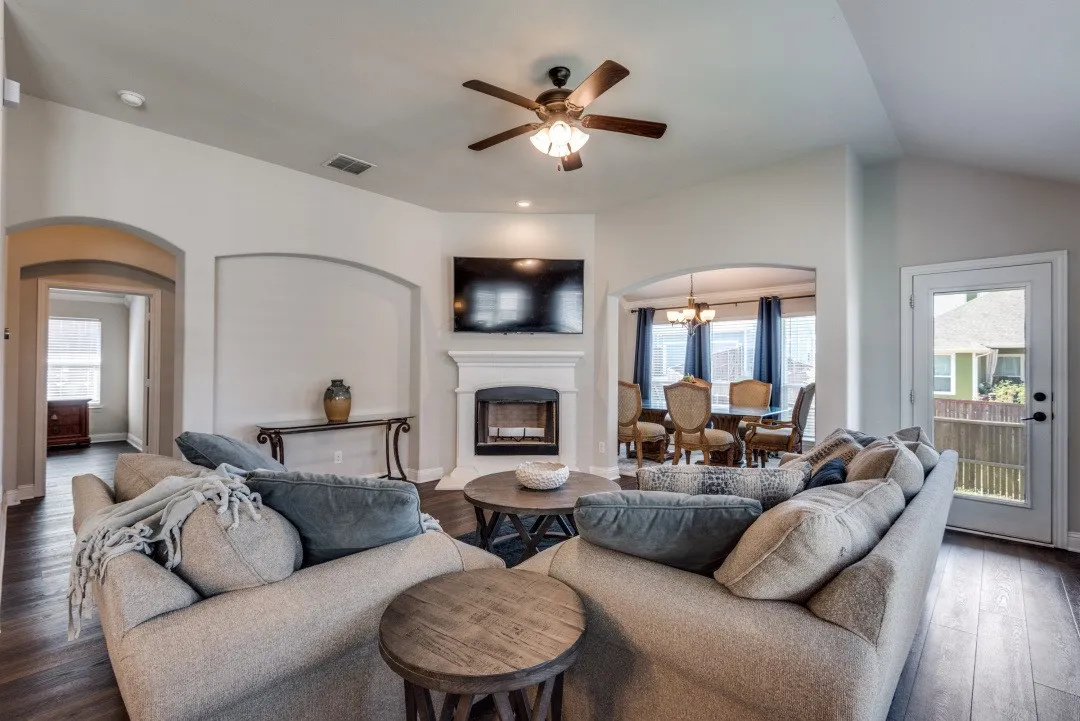 Vaulted ceiling with a ceiling fan, fireplace with a white mantel, arched doorways, wood-finish flooring, and a glass-paneled exterior door