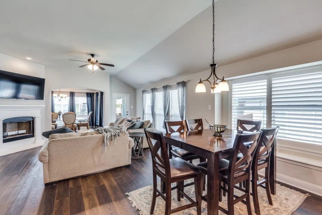 Expansive living area featuring wood-finish flooring, a white mantel fireplace, and a ceiling fan