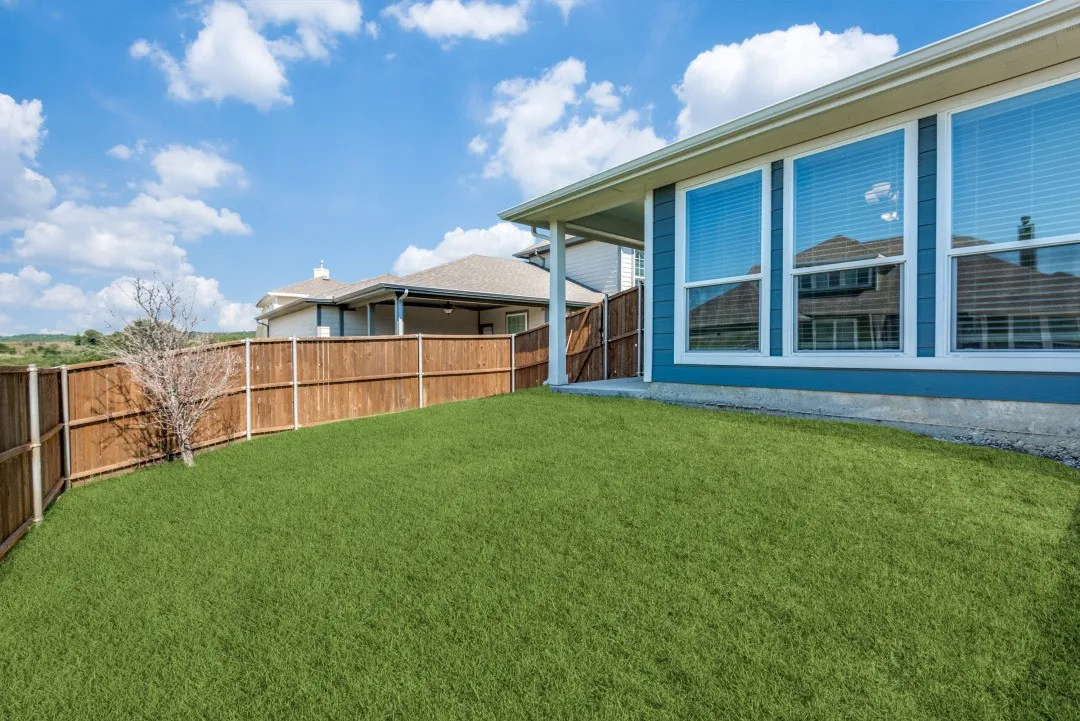 Spacious backyard featuring a wood privacy fence, covered patio, and multiple large windows