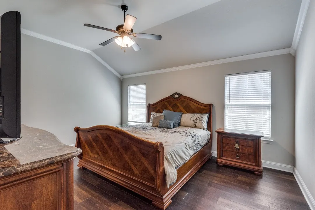 Vaulted ceiling with crown molding, wood-finish flooring, and two windows with blinds