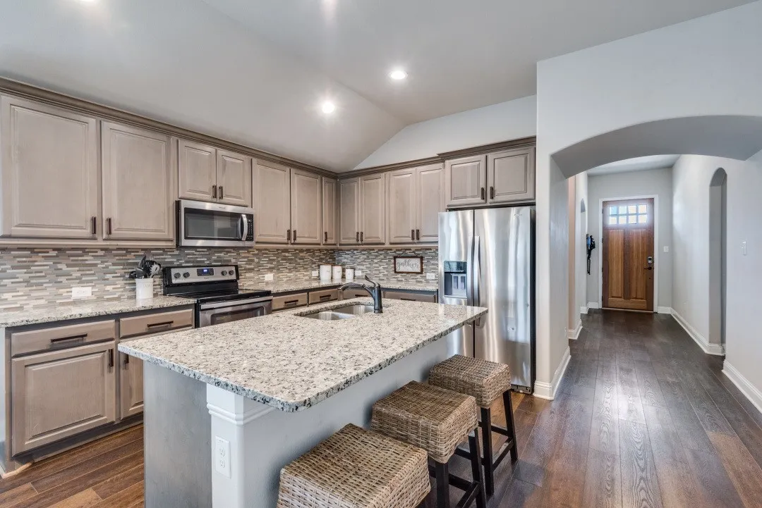 Kitchen featuring a large island with stone countertops, stainless steel appliances, extensive cabinetry, and a mosaic tile backsplash