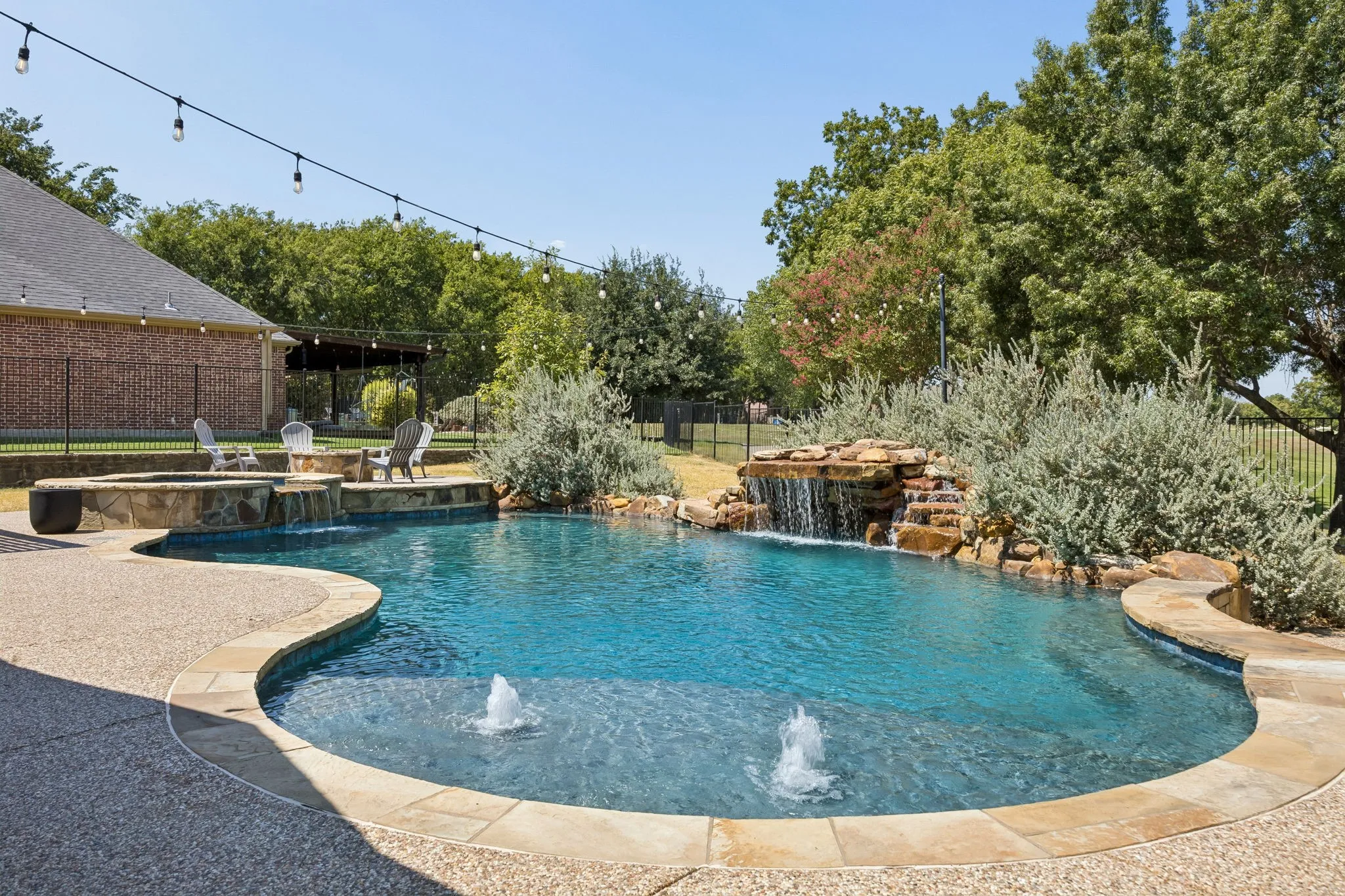 A Backyard Made for Summer - The freeform pool features a rock waterfall and shallow entry area, creating a resort-like setting with plenty of surrounding deck space for lounging and gathering.