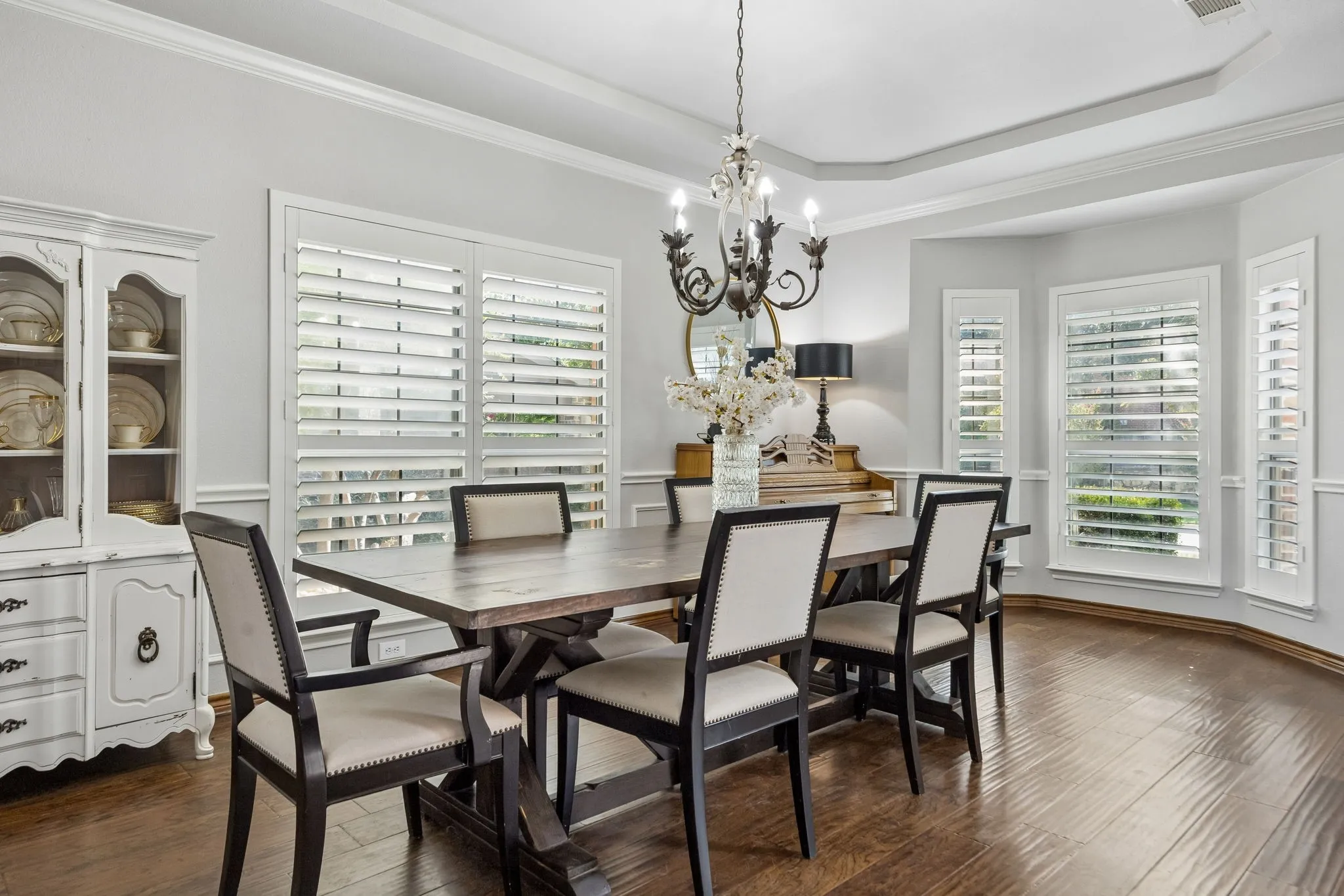 Bright Formal Dining - Multiple windows with plantation shutters bring natural light into the dining room, while detailed millwork and warm hardwood flooring give the space architectural character.