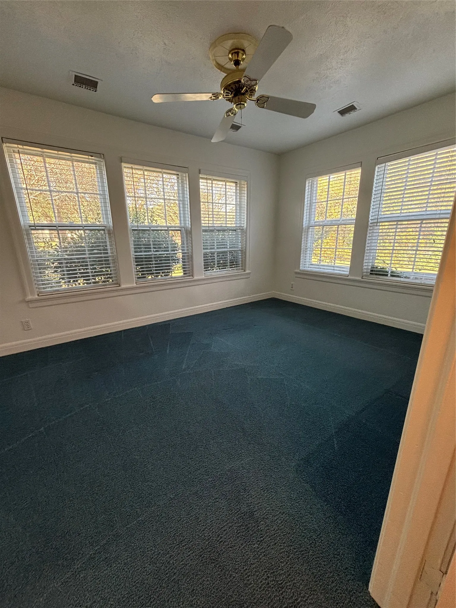 Spare room with a textured ceiling, dark carpet, and ceiling fan