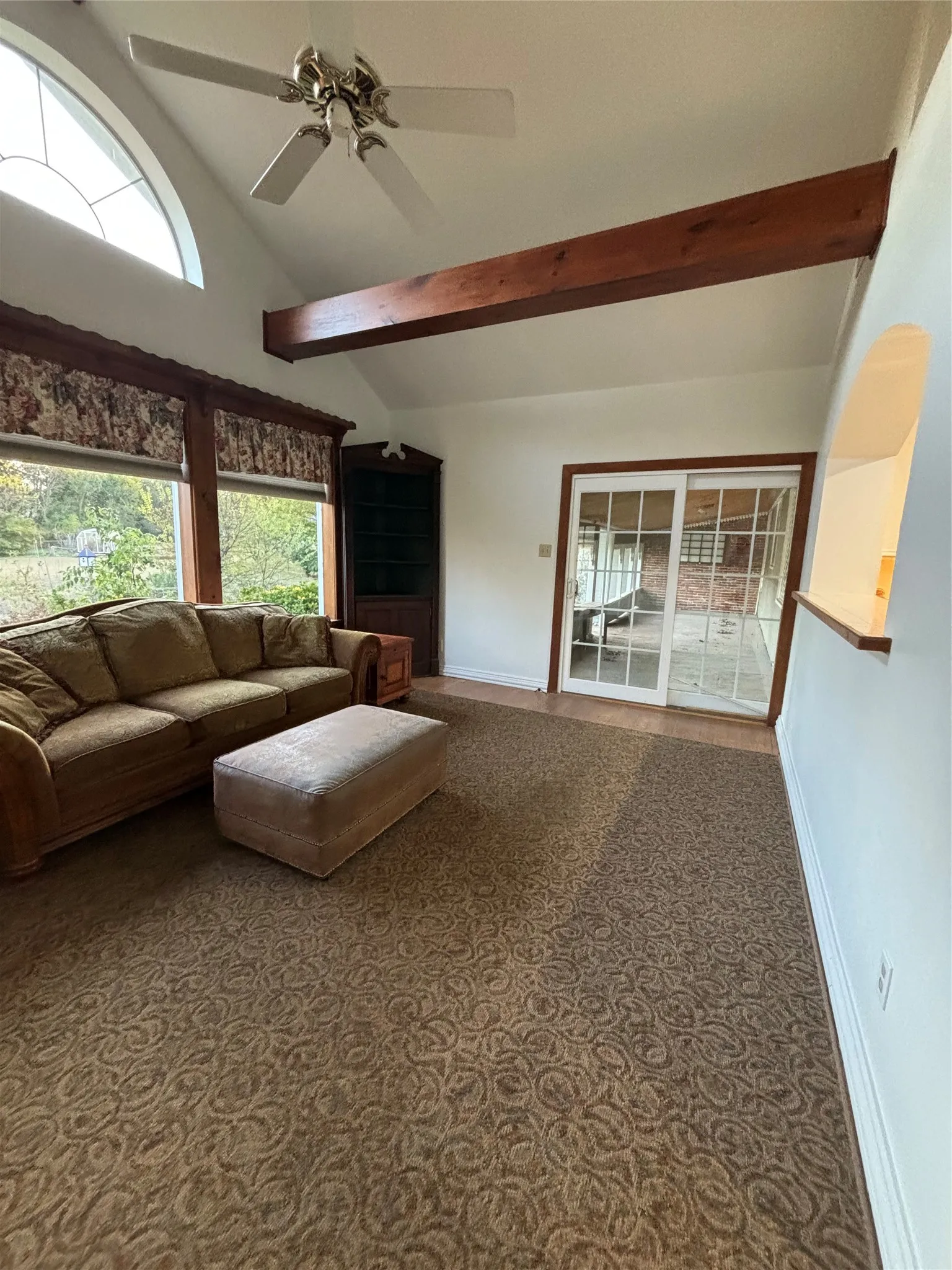 Carpeted living room featuring healthy amount of natural light, beamed ceiling, ceiling fan, and high vaulted ceiling
