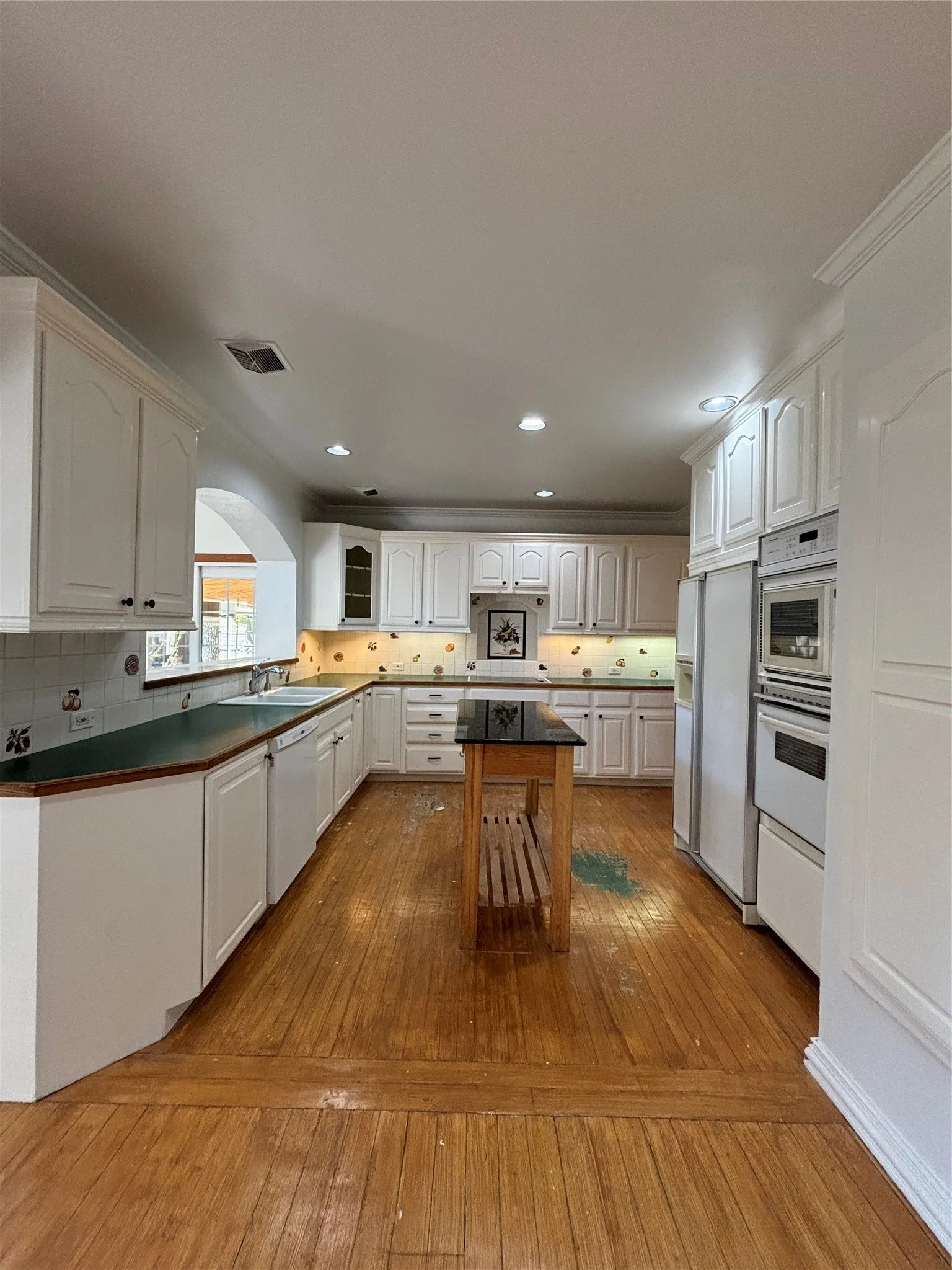 Kitchen with light wood finished floors, backsplash, white cabinets, dark countertops, and refrigerator