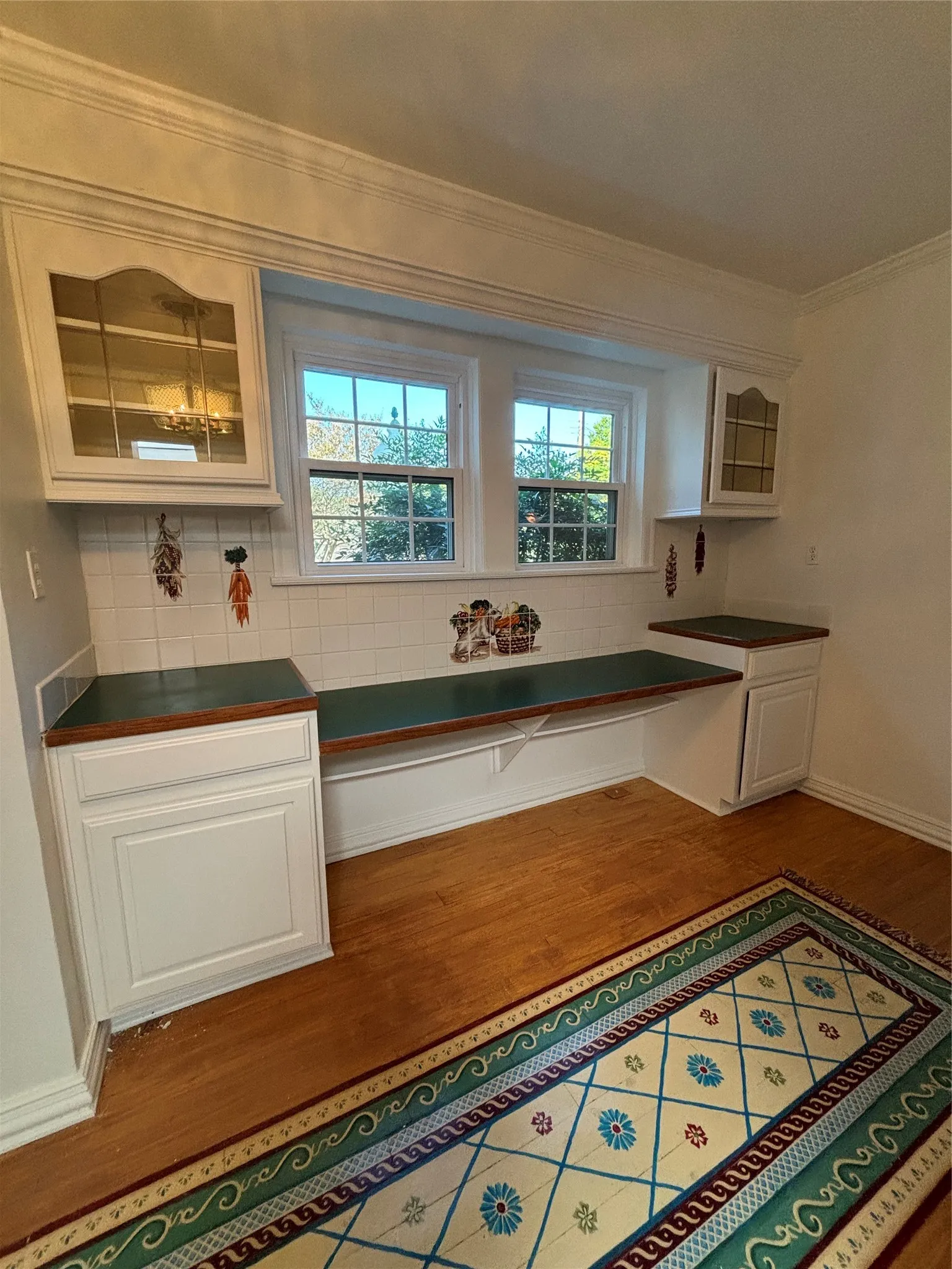 Kitchen with white cabinetry, glass insert cabinets, backsplash, dark countertops, and ornamental molding