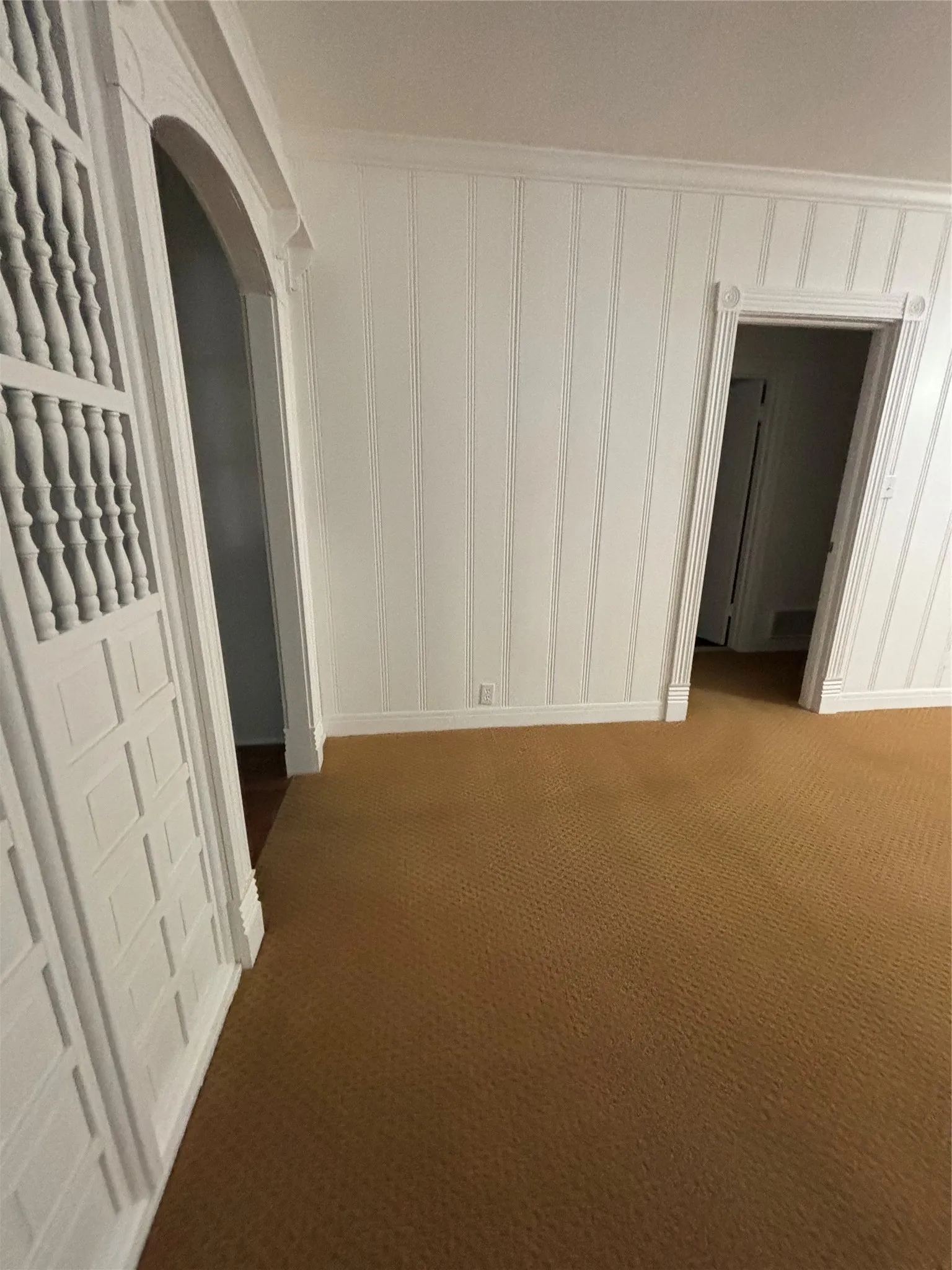 Separation between the formal living room & formal dining room featuring arched walkways and dark carpet