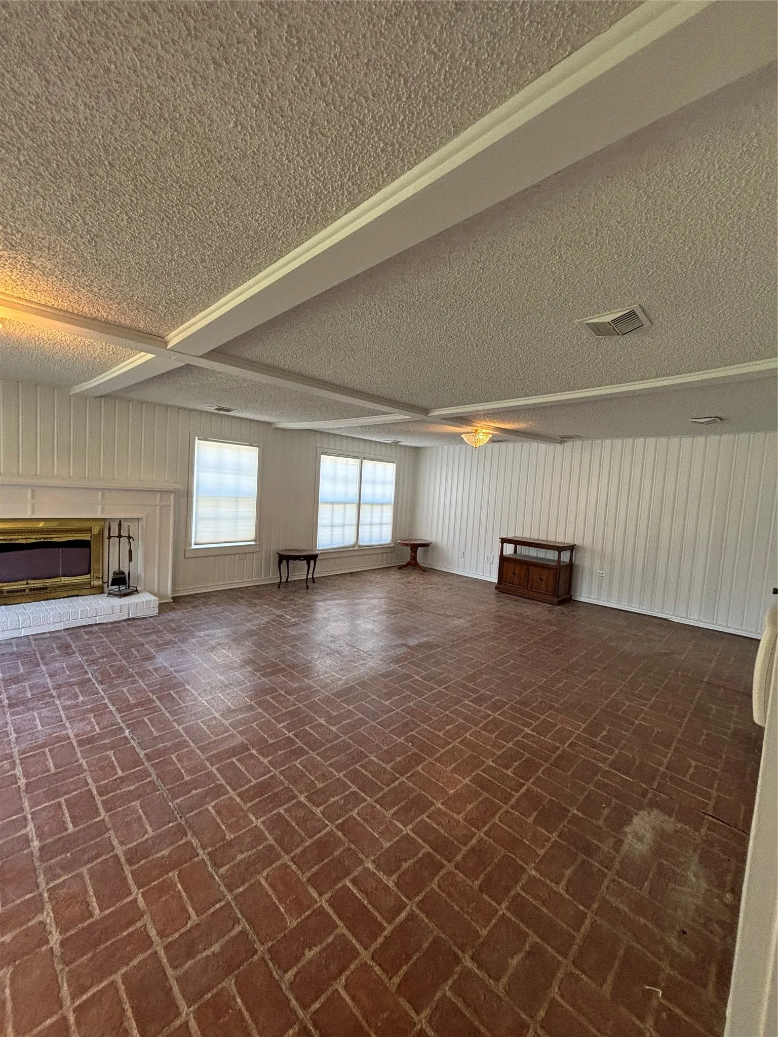 Unfurnished living room featuring a glass covered fireplace, a textured ceiling, and brick patterned floors