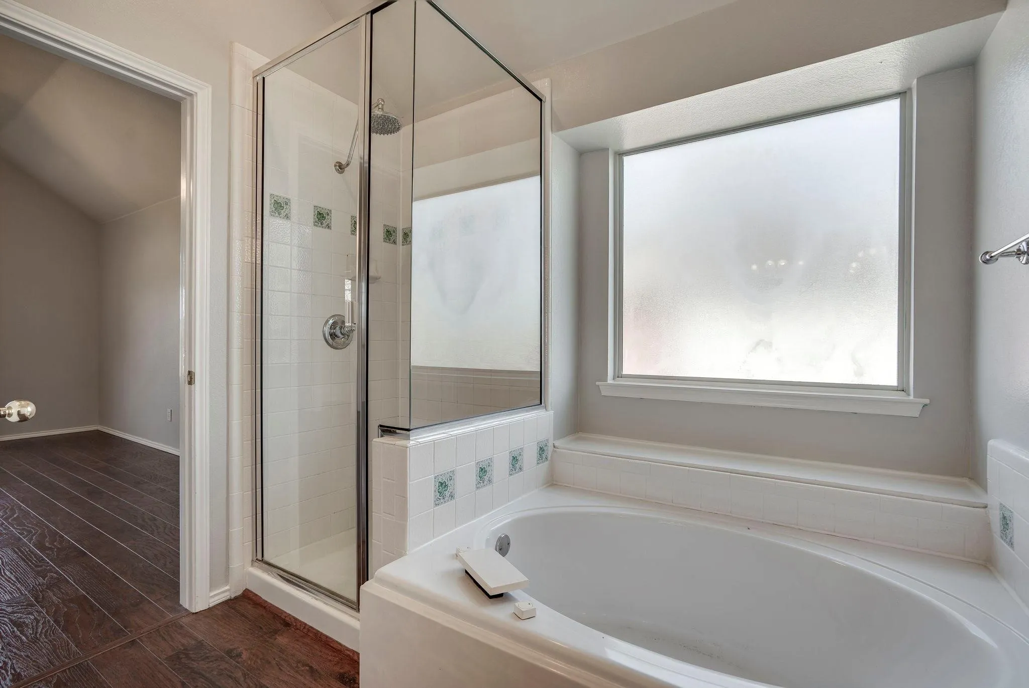 Built-in soaking tub, separate glass-enclosed shower, white tile surround with decorative accents, and a frosted window