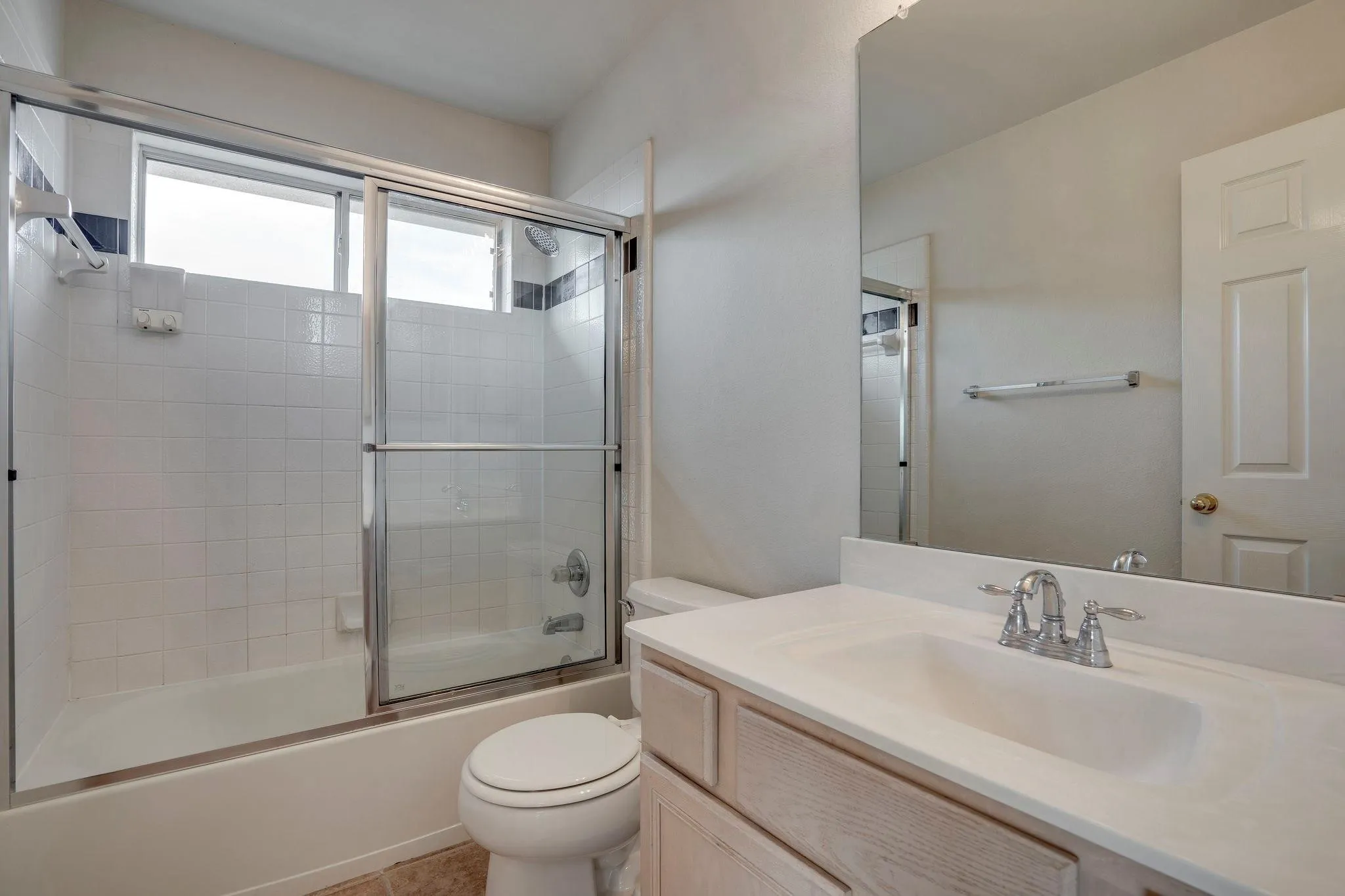 Bathtub and shower combination with sliding glass doors, white tiled surround, single vanity with integrated sink, and wall-mounted mirror