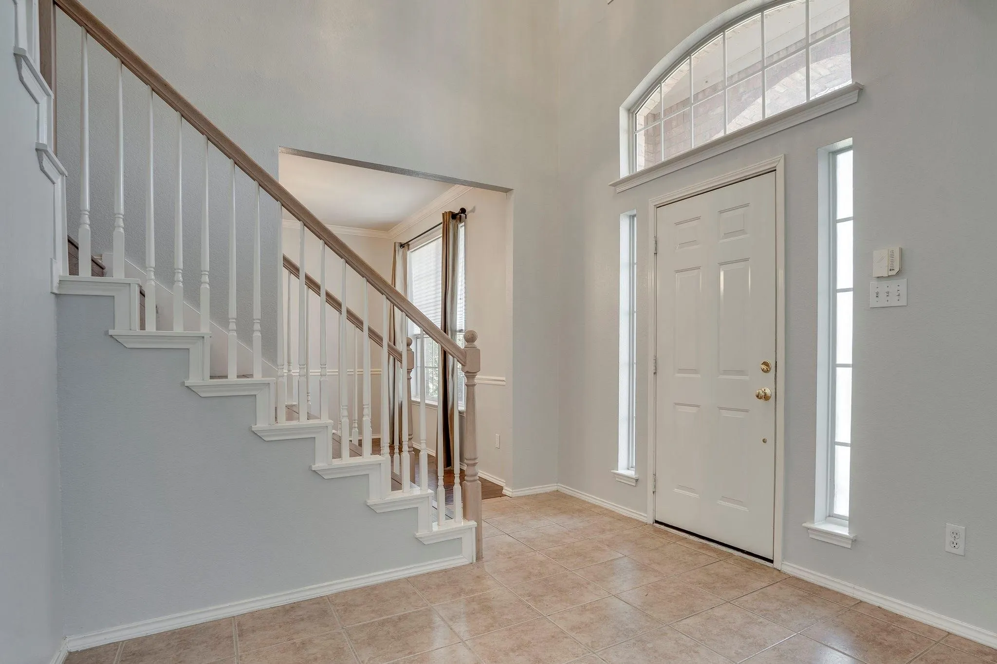 Two-story foyer with high ceilings, ceramic tile flooring, a staircase featuring painted risers and balusters with a wood-finish handrail, and a front entry door with transom and sidelight windows