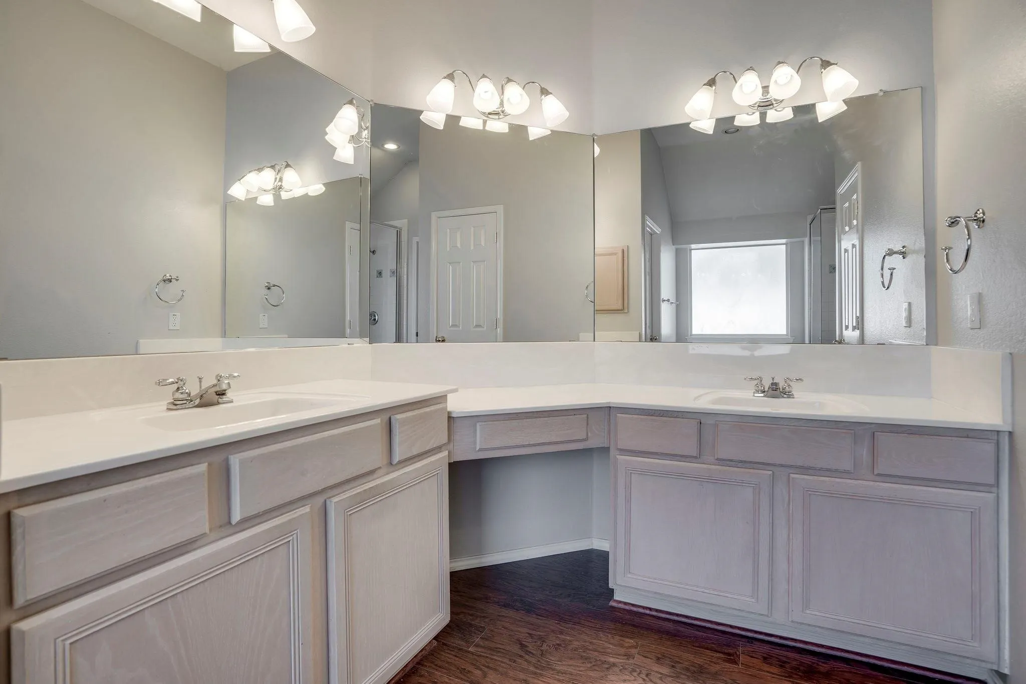 Dual vanity with integrated sinks, expansive counter space, wood-finish flooring, and wall-mounted lighting fixtures
