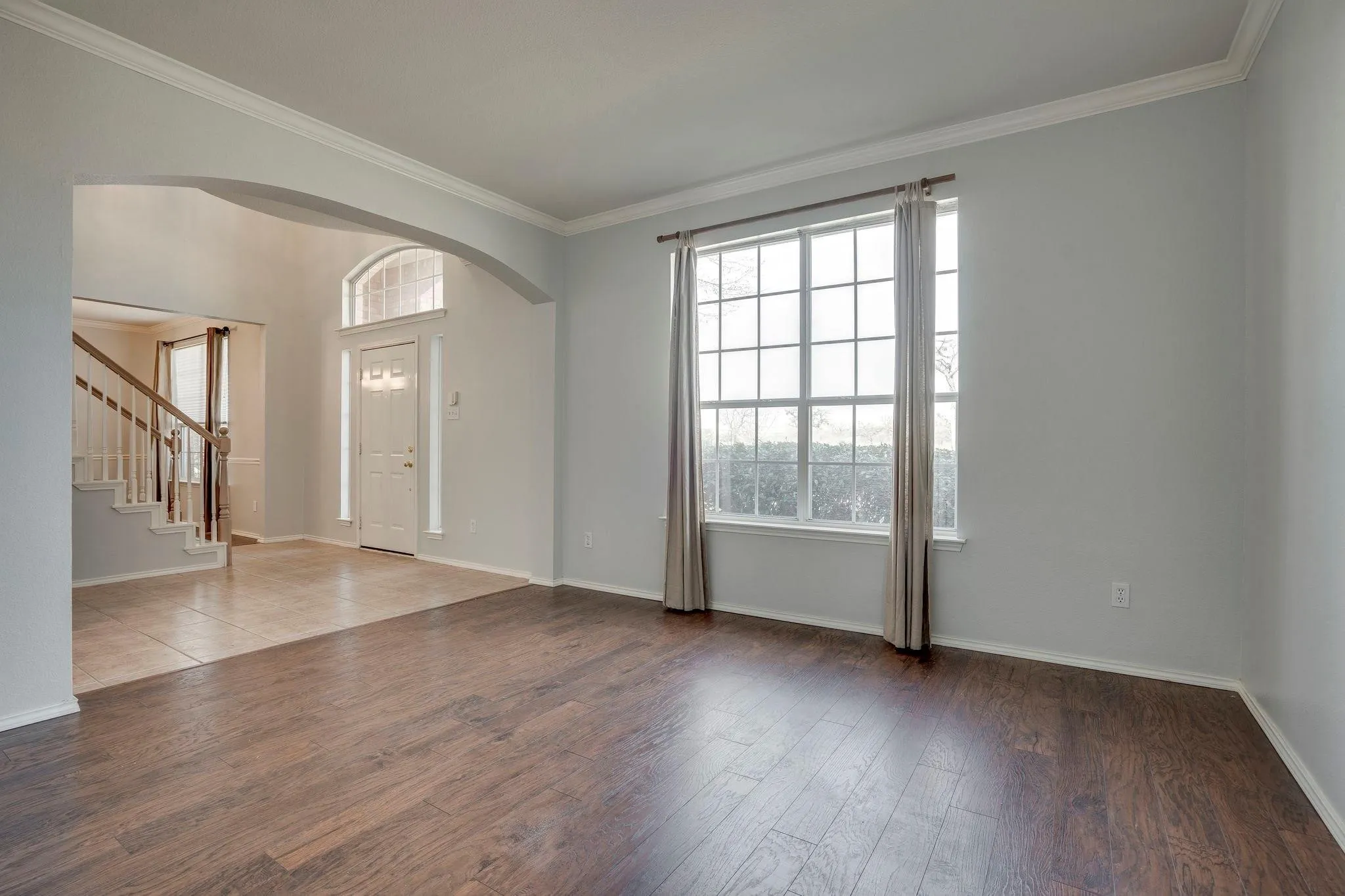 Wood-finish flooring, arched entryway, large window with grid pattern, light gray wall paint, and crown molding
