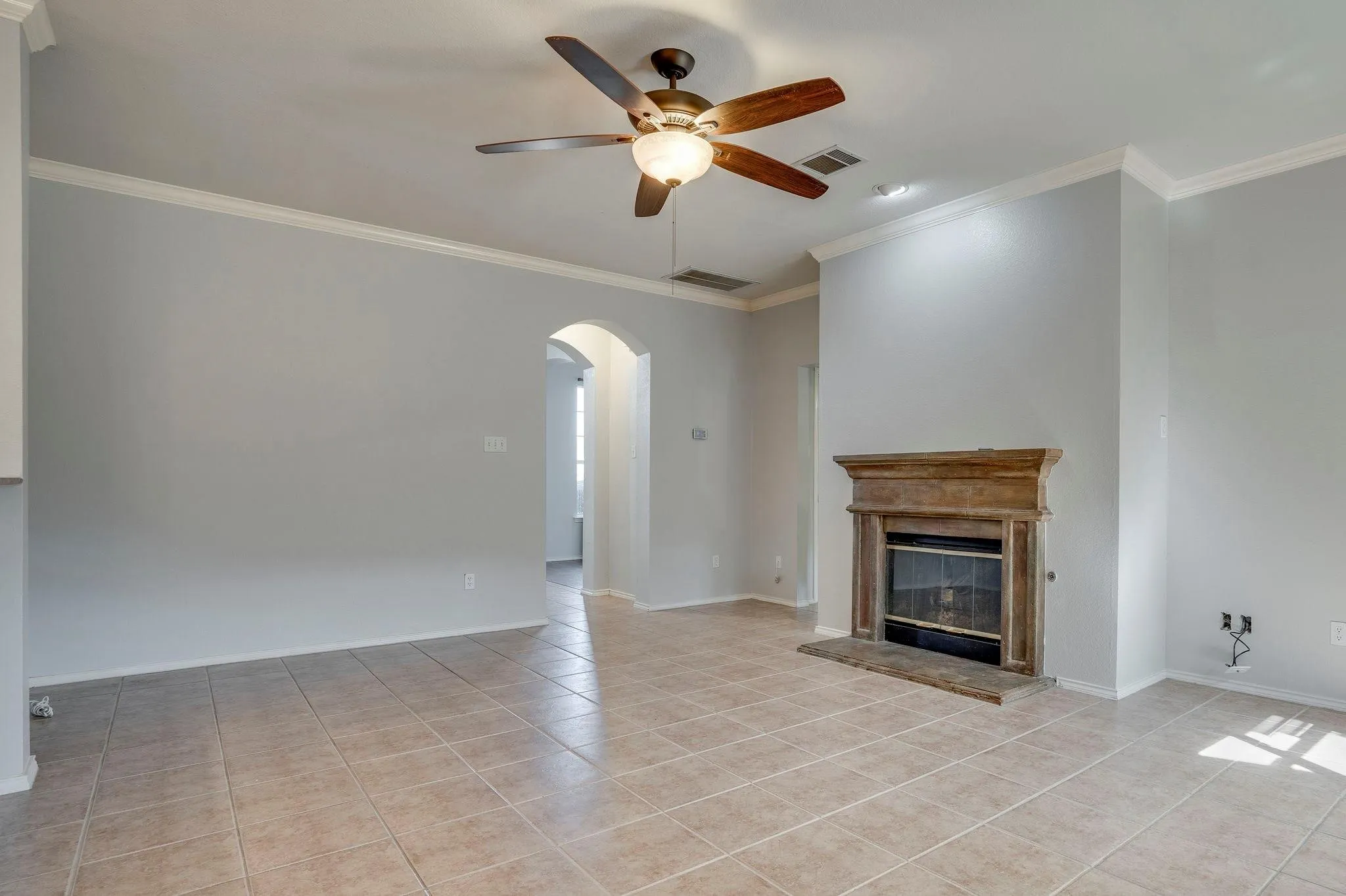 Tiled flooring, crown molding, arched entry, built-in fireplace with mantel, and ceiling fan with integrated lighting