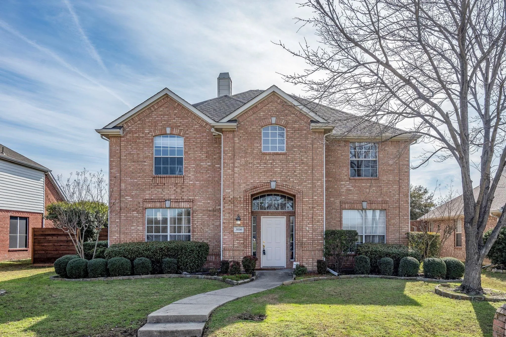Brick-clad exterior with white trim, arched entryway, and mature landscaping
