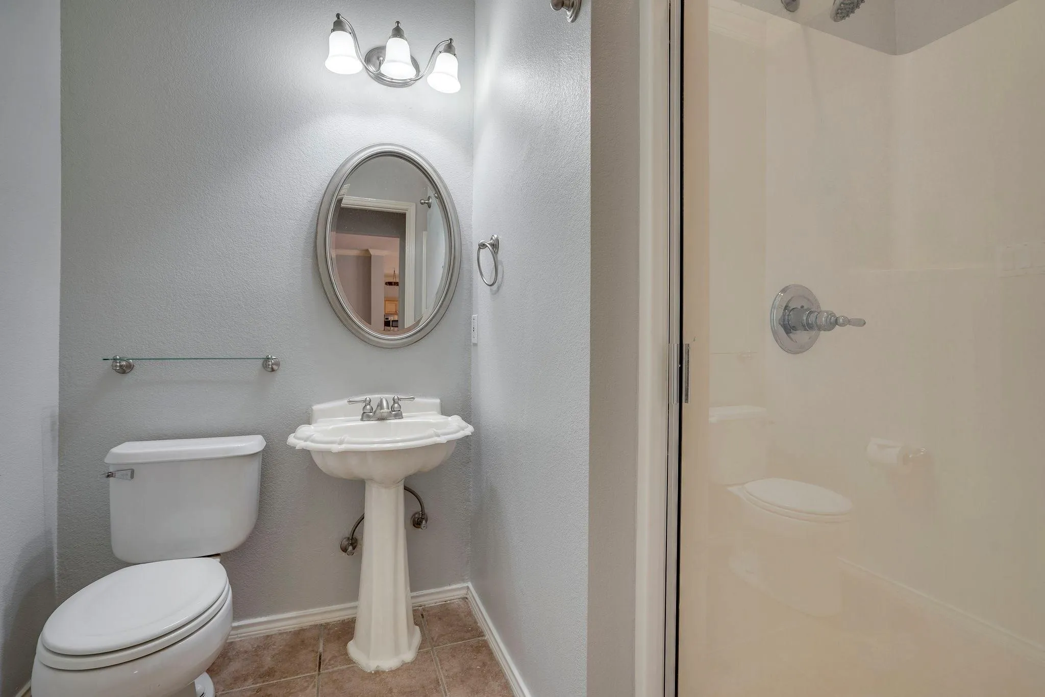 Pedestal sink with chrome fixtures, oval mirror, and three-light vanity fixture