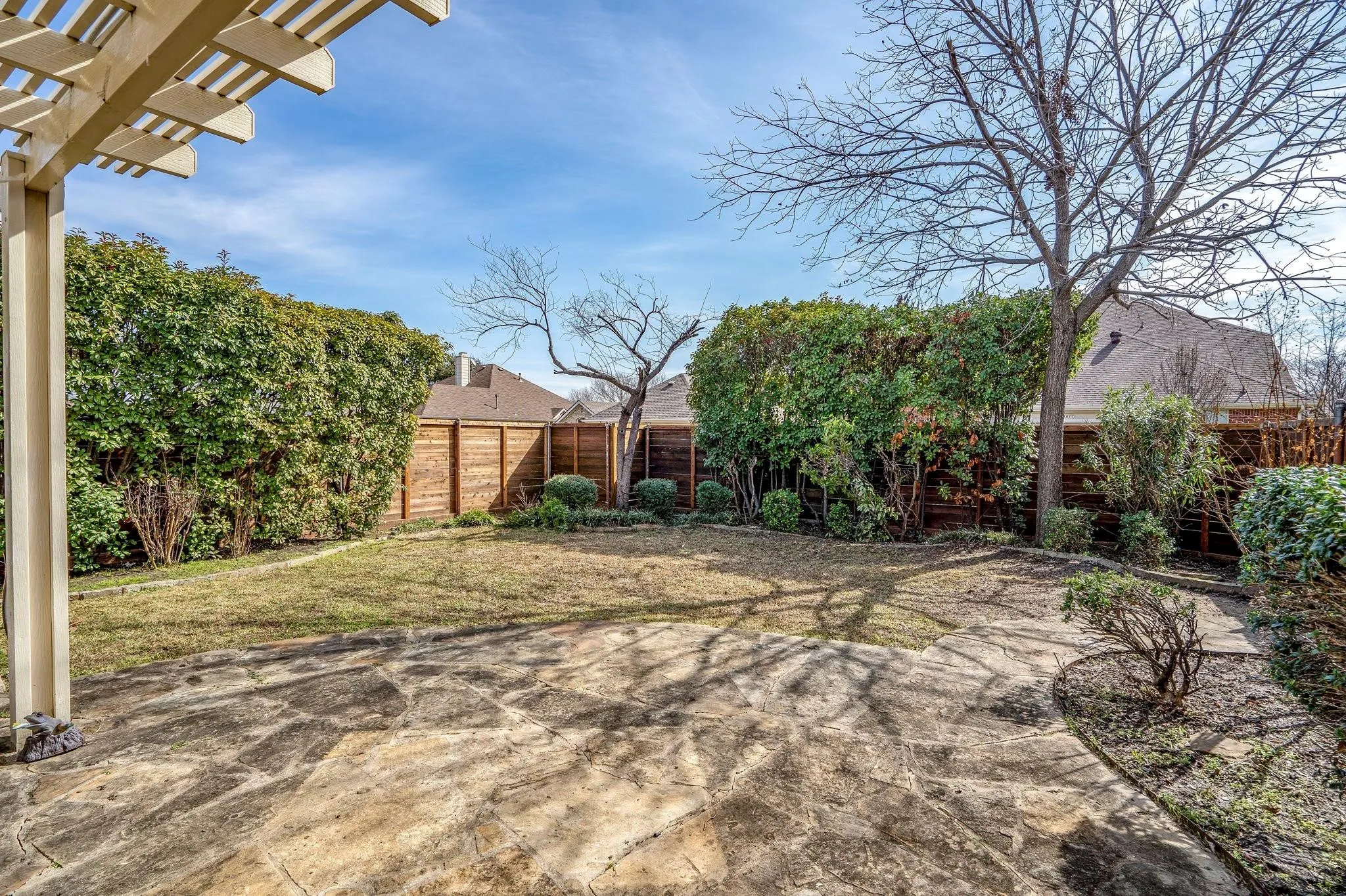 Expansive backyard featuring a stone patio, manicured lawn, and mature privacy shrubs
