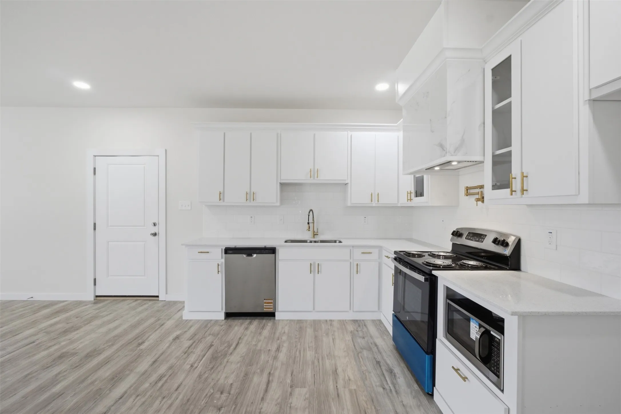 Bright kitchen featuring white cabinetry, light countertops, wood-finish flooring, and stainless steel appliances