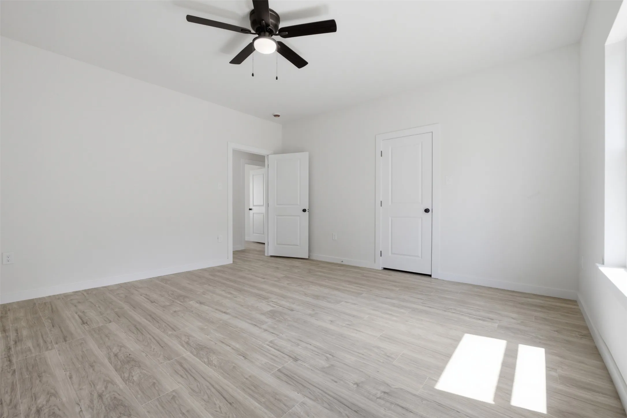 Spacious room featuring wood-finish flooring, a contemporary ceiling fan, and white paneled doors
