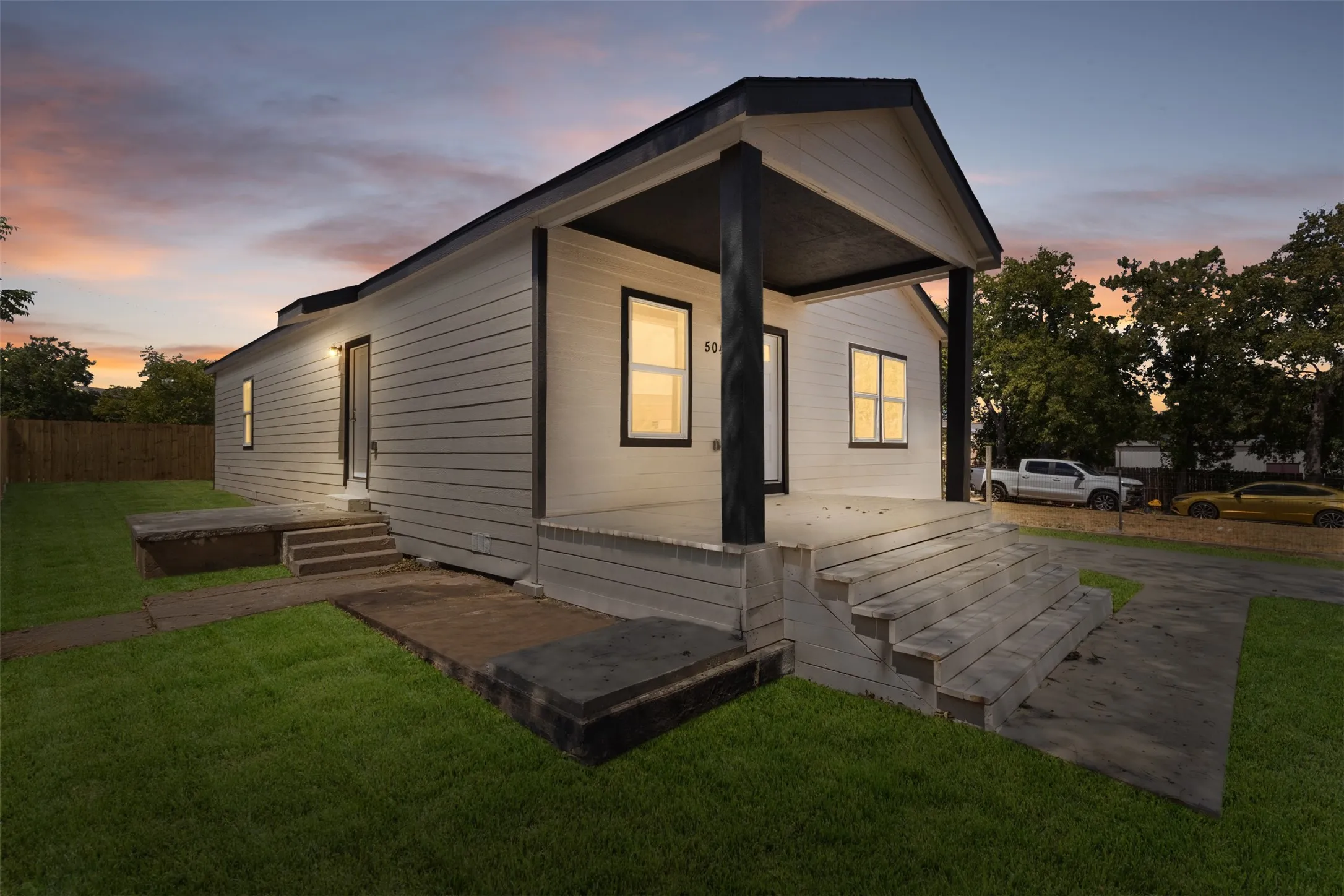 Exterior featuring white horizontal siding, black trim windows, a covered front porch, and a well-maintained lawn