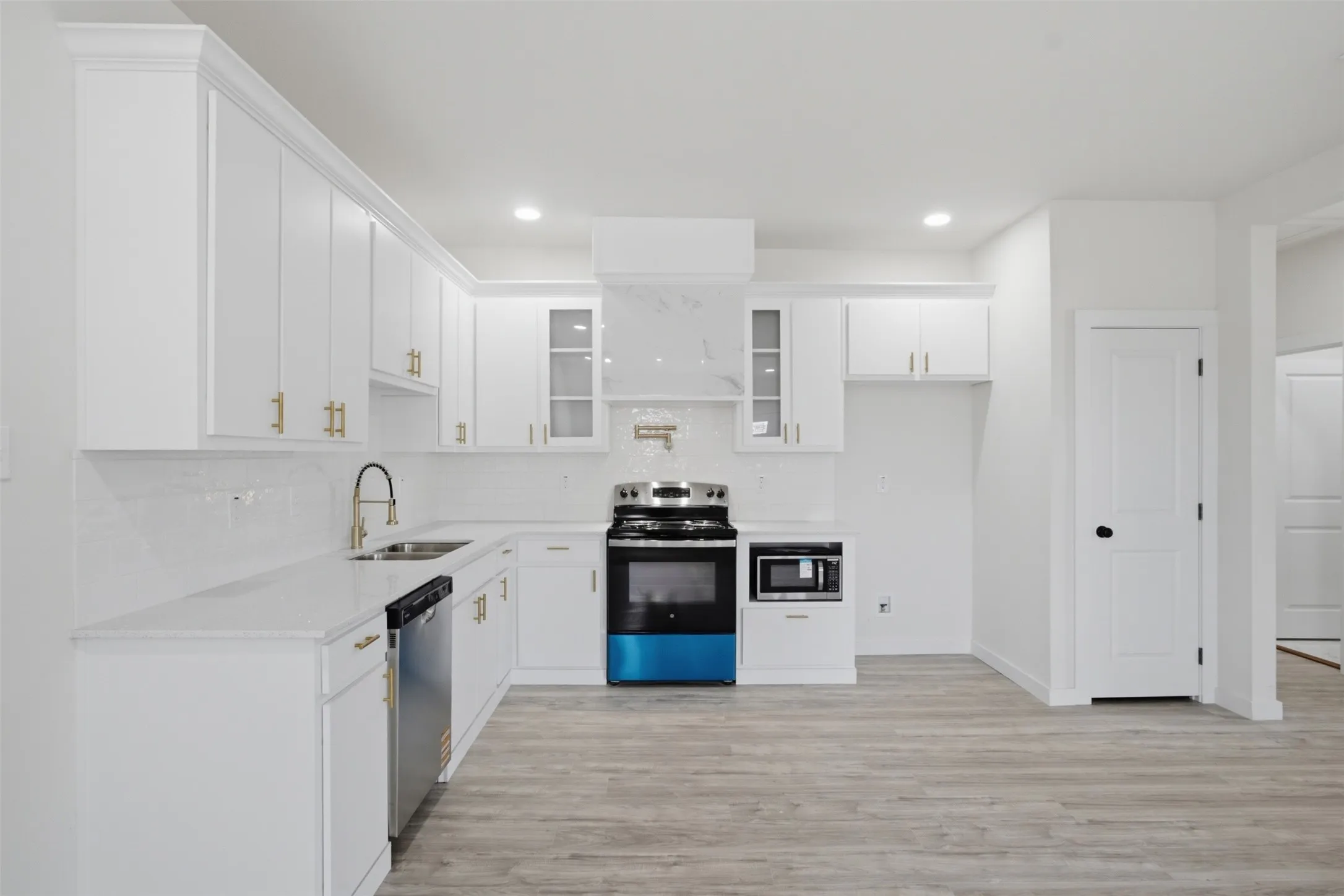 White shaker-style cabinetry, stainless steel appliances, solid surface countertops, white subway tile backsplash, and light wood-finish flooring