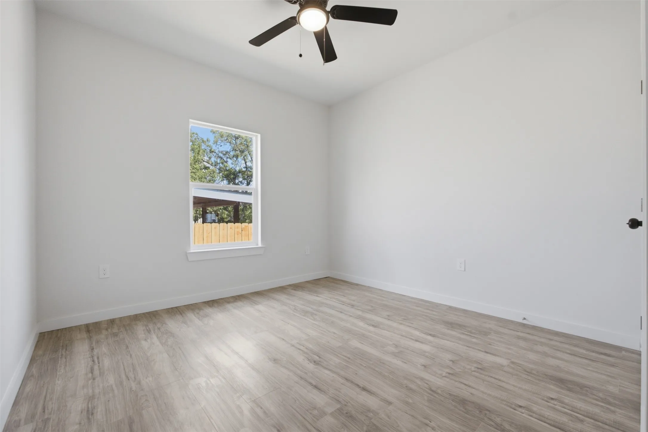 Spacious room featuring wood-finish flooring, a ceiling fan, and a single window