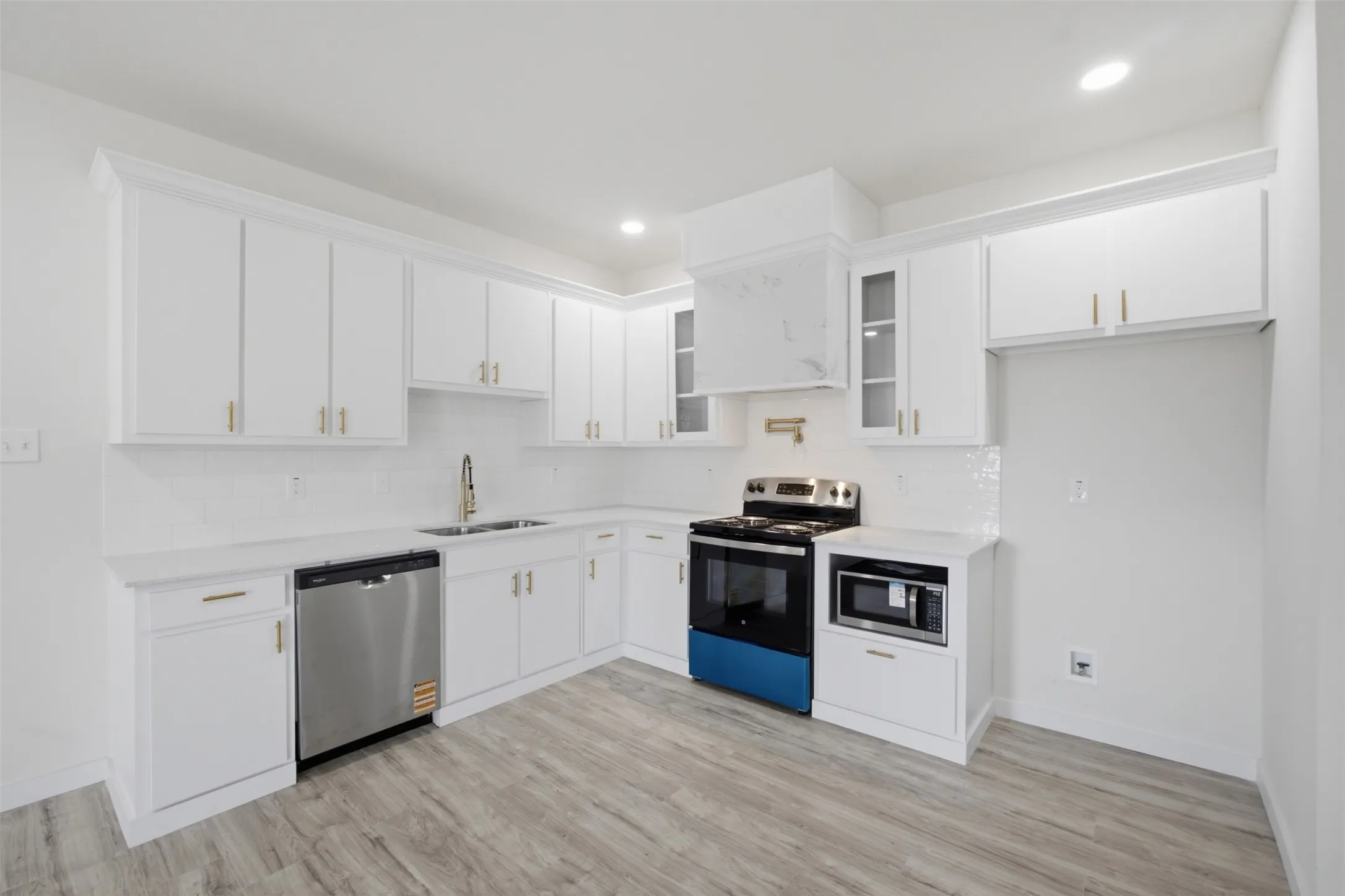 White cabinetry, stainless steel appliances, light-toned wood-finish flooring, white countertops, and recessed lighting