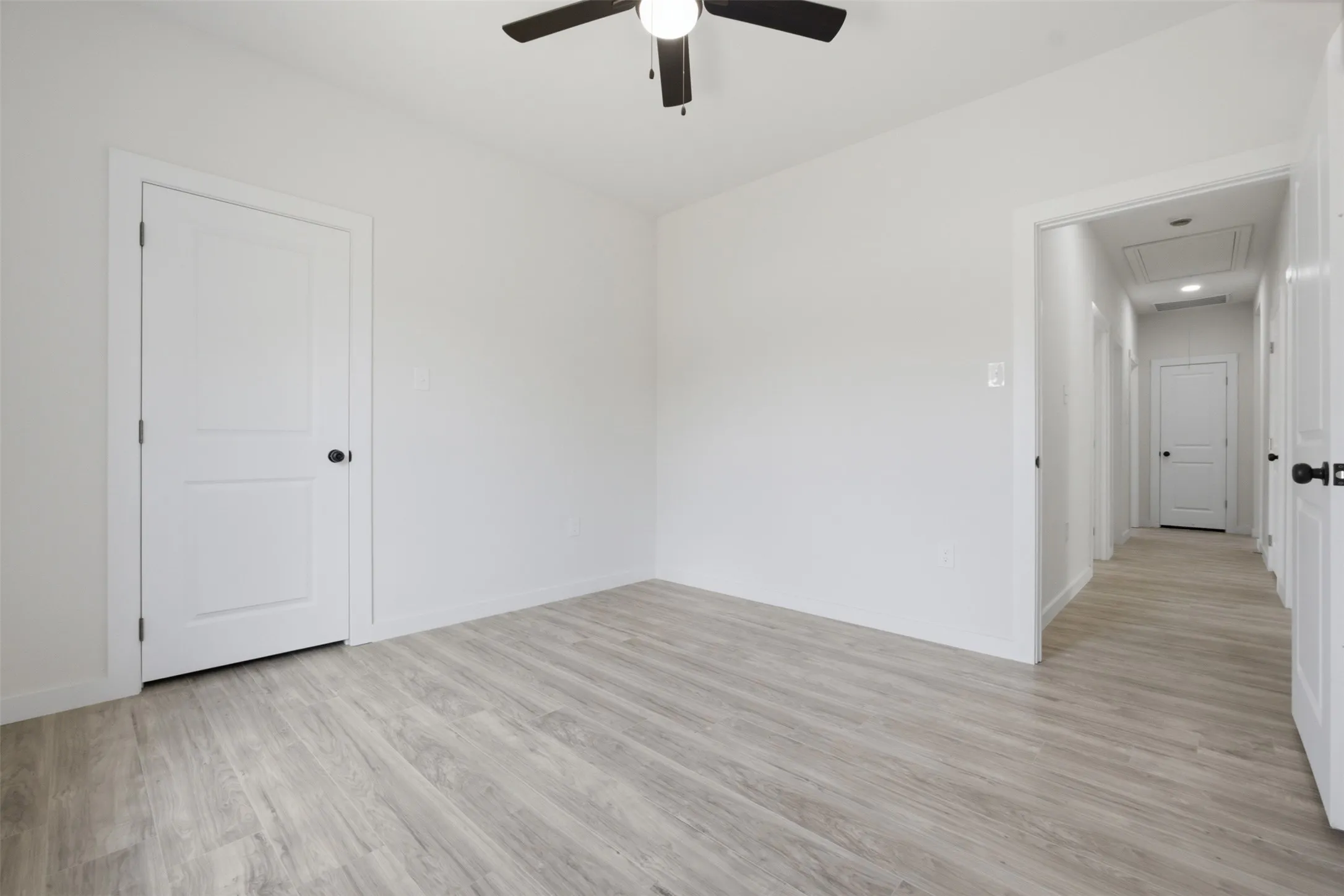 Wood-finish flooring, white walls, white two-panel doors, and a ceiling fan with integrated lighting