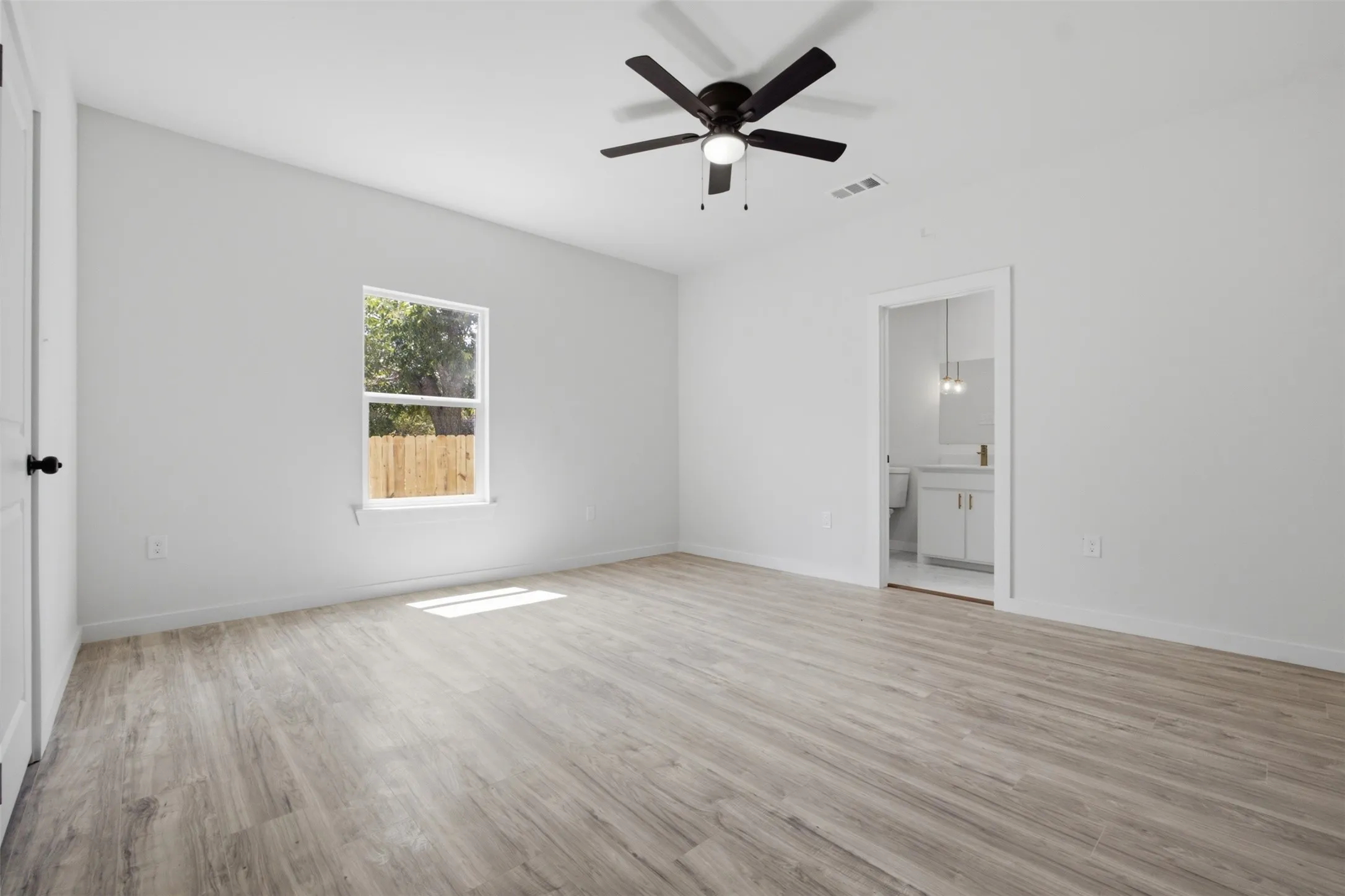 Spacious room featuring wood-finish flooring, a ceiling fan with integrated lighting, and a window with a wood fence backdrop