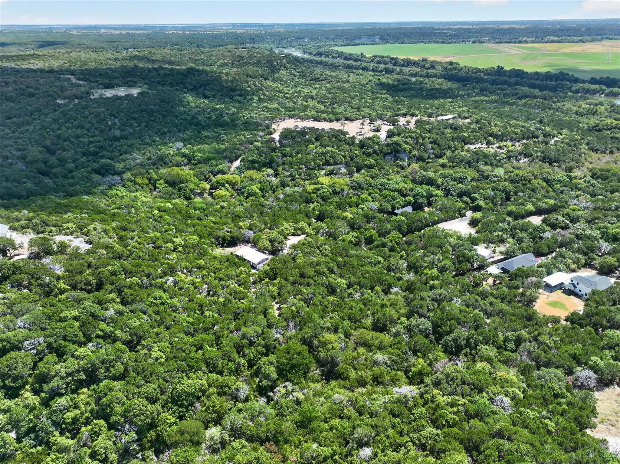 Expansive natural landscape featuring dense tree coverage, distant open fields, and scattered residential structures