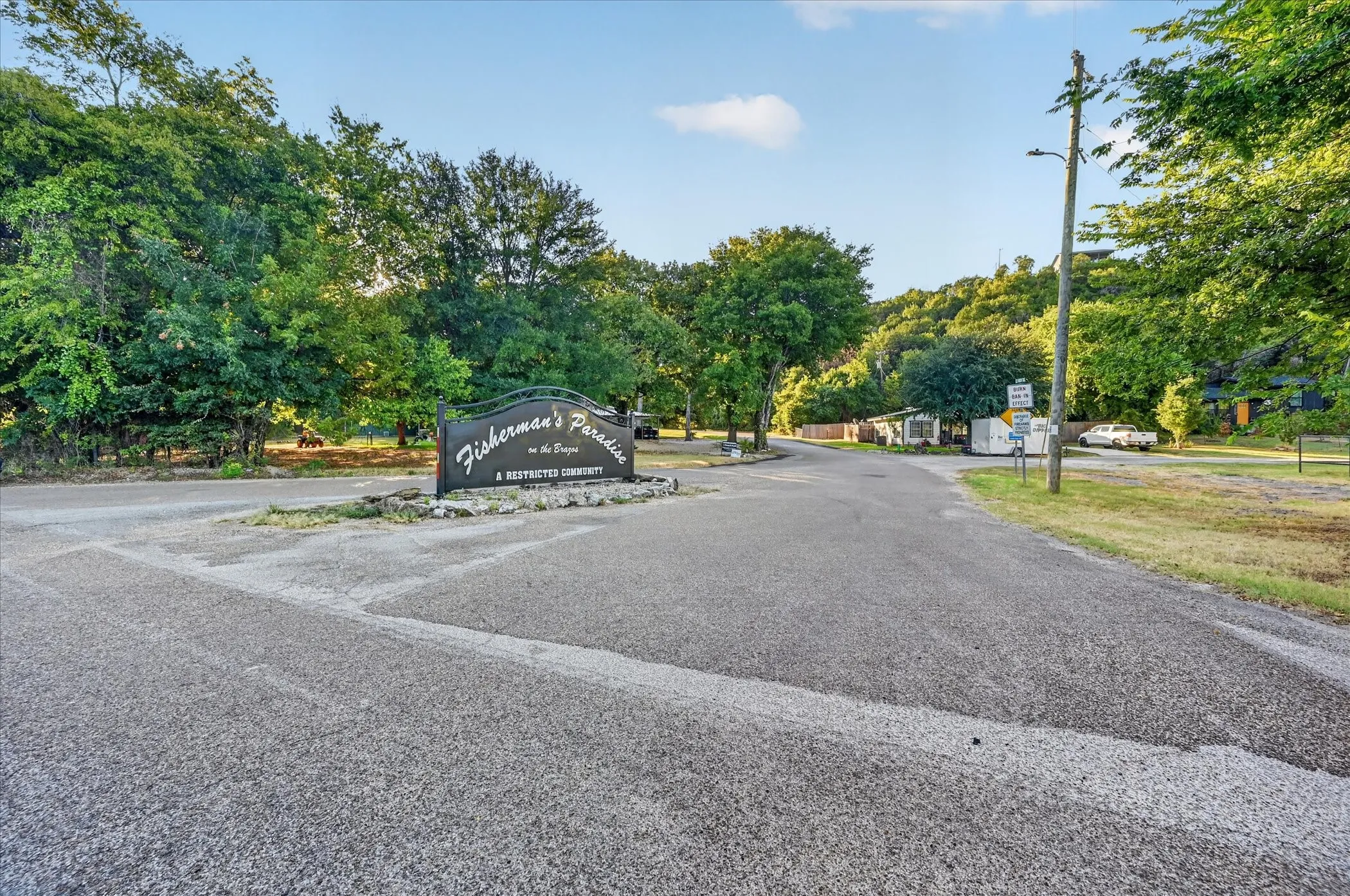 Entry sign with stone base, paved road, and mature trees