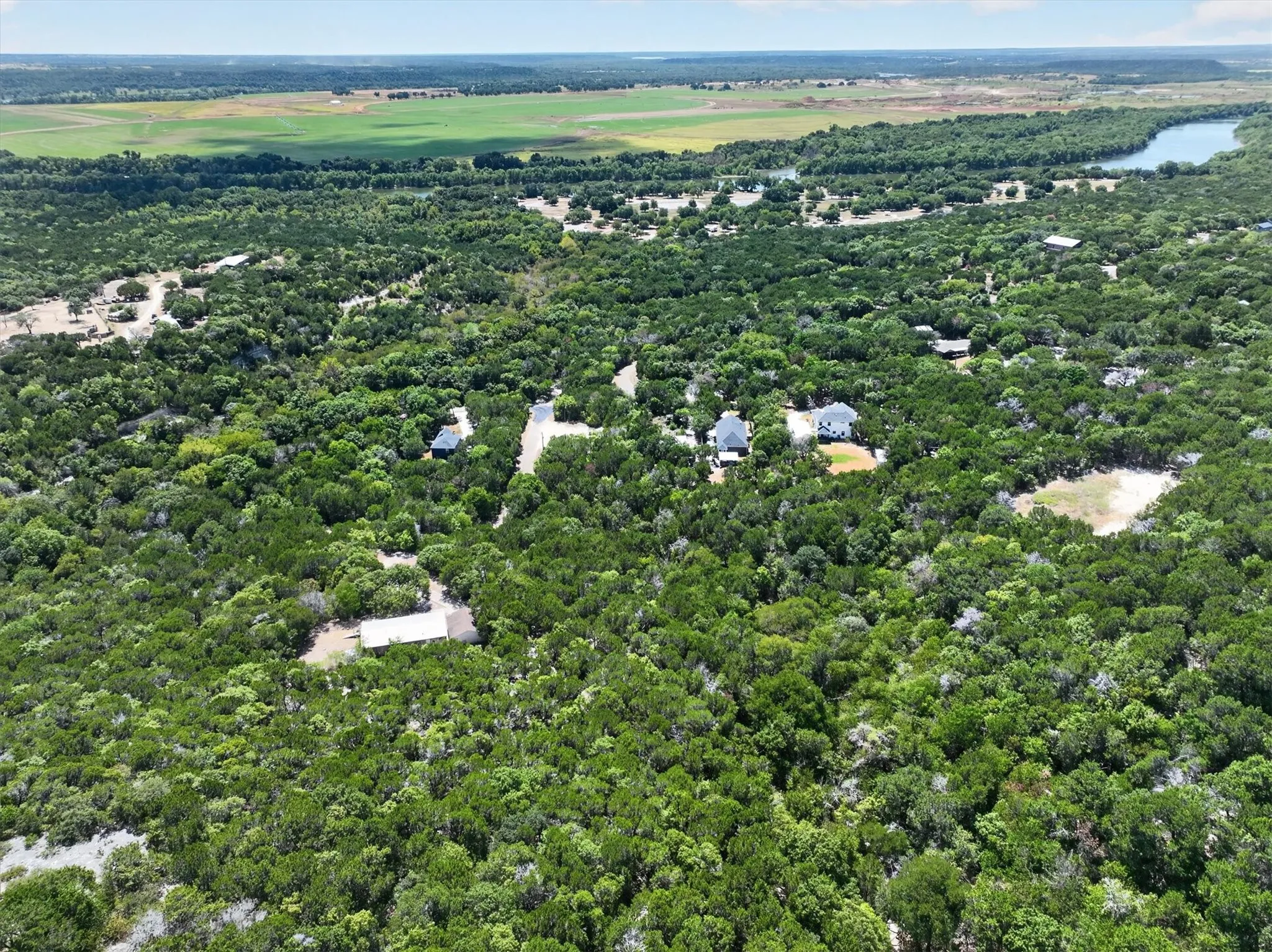 Expansive wooded landscape featuring mature trees, multiple residential structures, and a prominent water body in the background