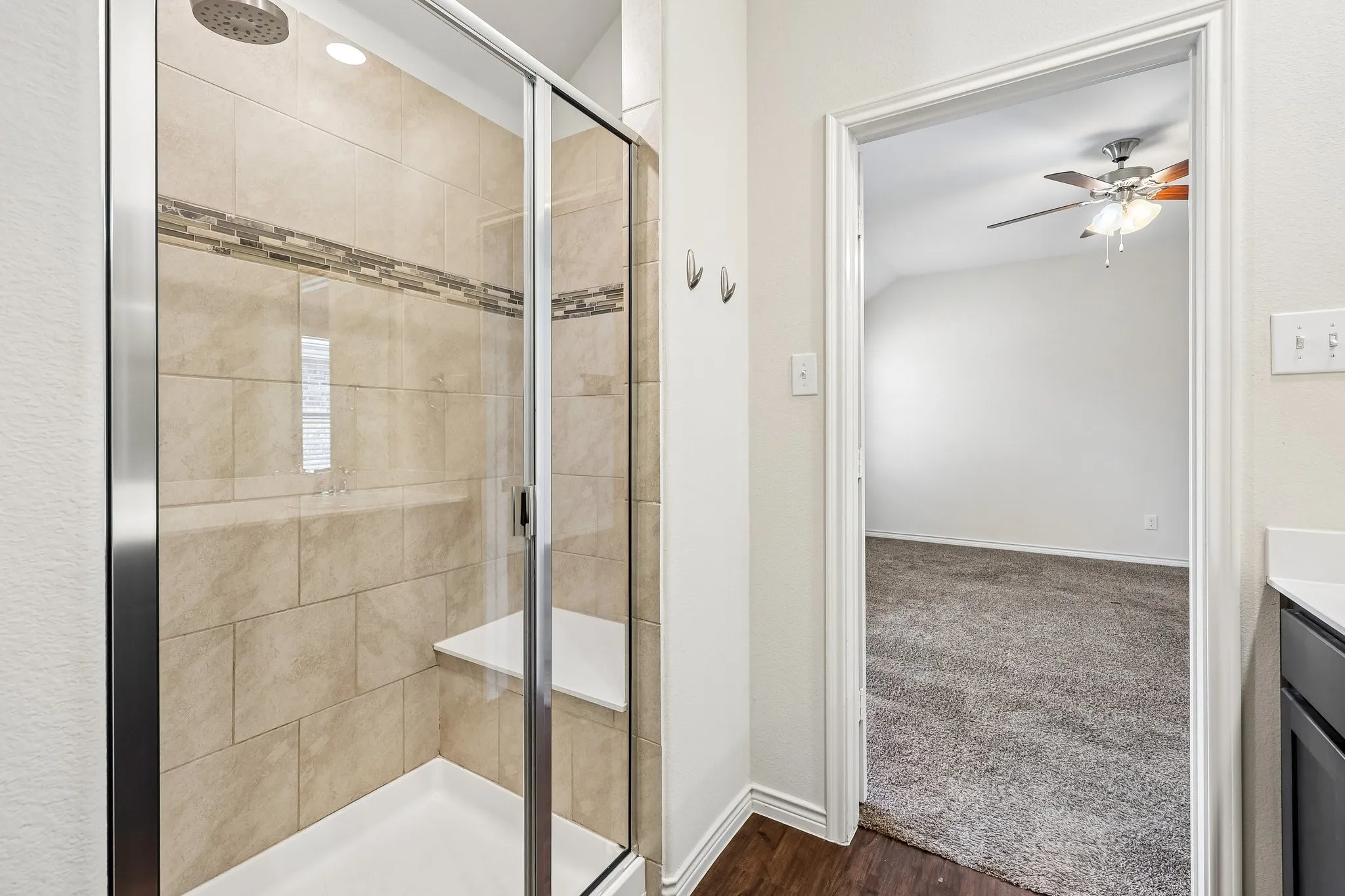 Glass-enclosed shower with a built-in bench, tiled walls, and decorative mosaic accent band
