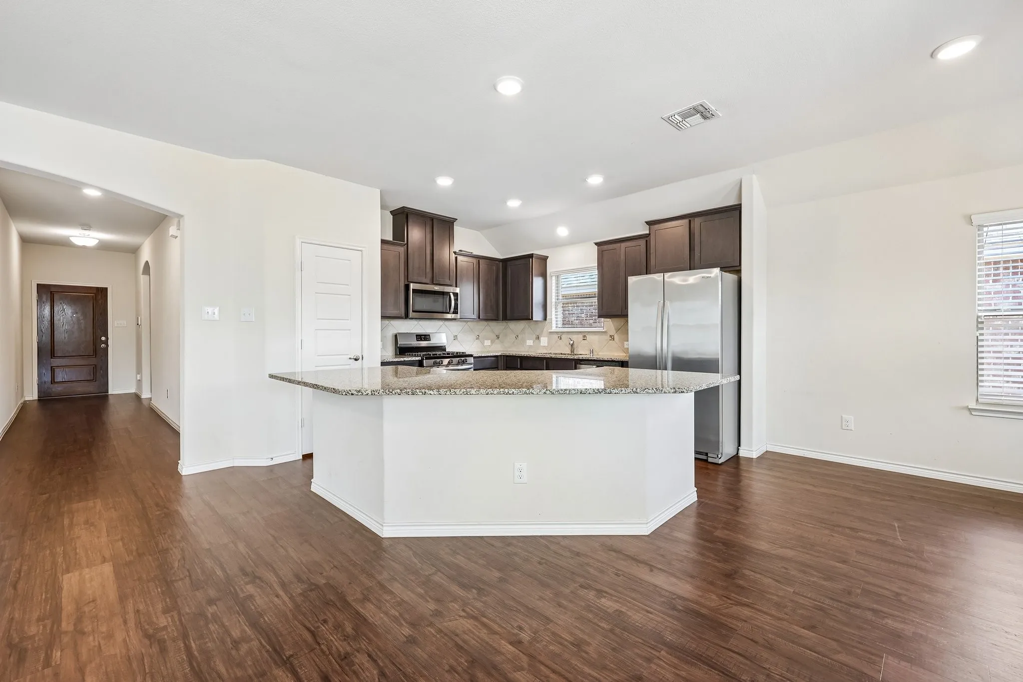 Kitchen featuring dark wood cabinetry, stainless steel appliances, a tile backsplash, and a breakfast bar with a light-toned countertop