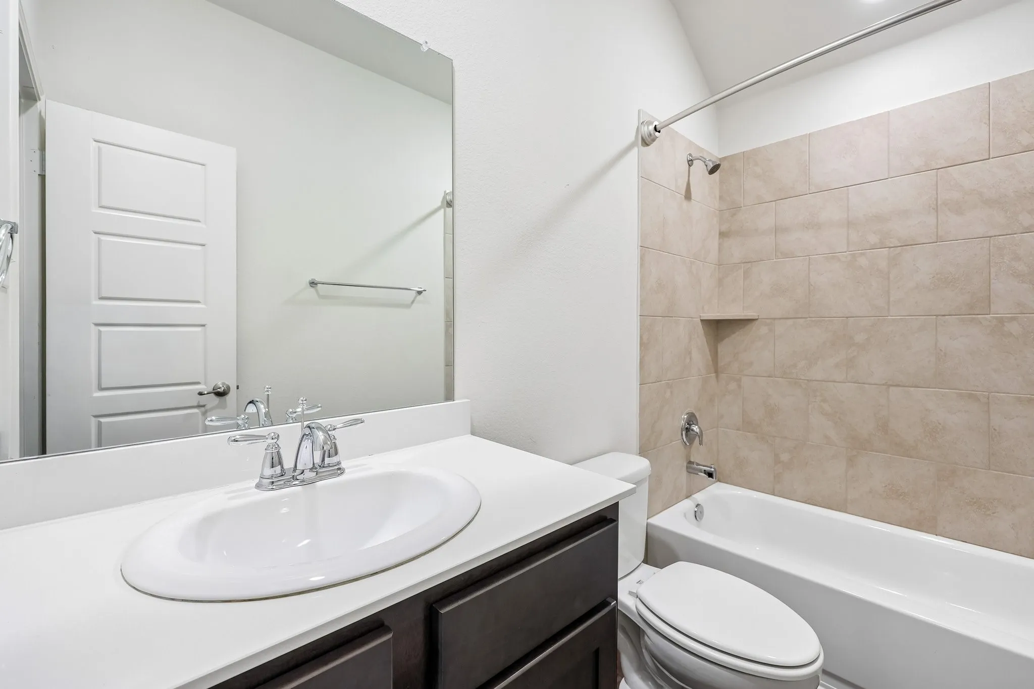 Bathroom featuring a built-in tub with tile surround, integrated shower niche, and a vanity with an undermount sink and chrome fixtures