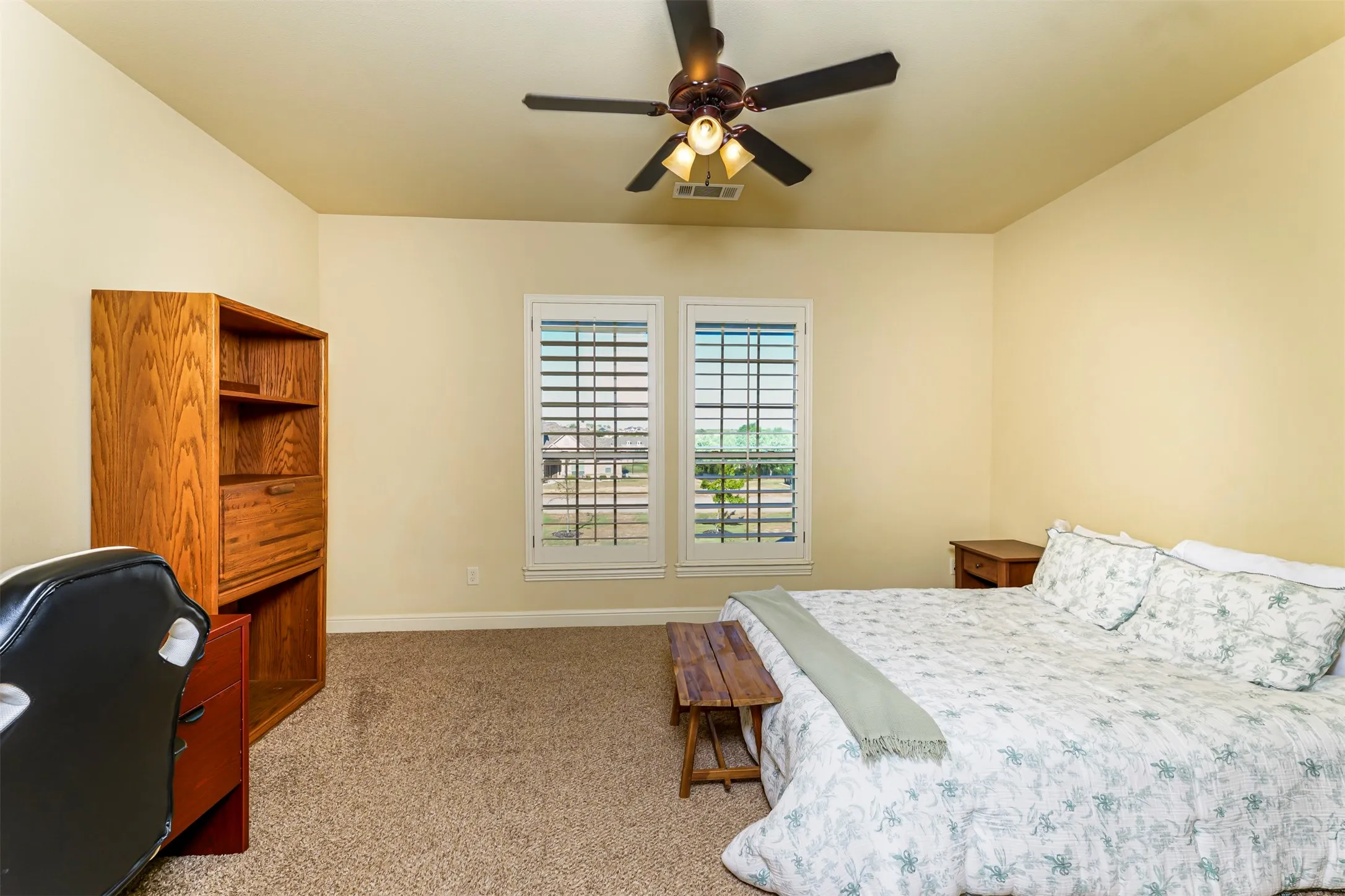 Vaulted ceiling with a ceiling fan, carpet flooring, dual windows with plantation shutters, and a built-in wood shelving unit