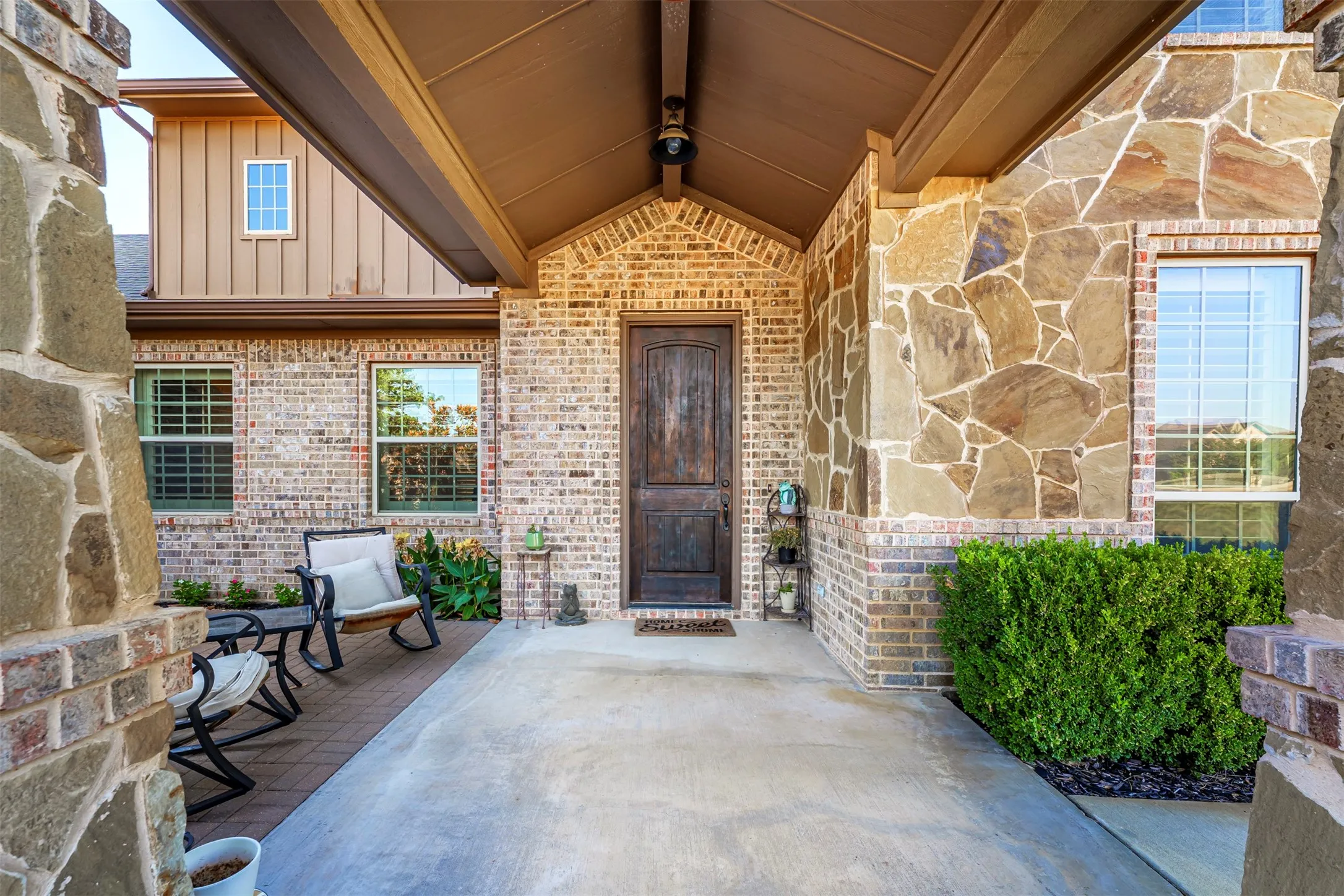 Covered entry with a wood-finish front door, stone and brick facade, and an adjacent paved patio