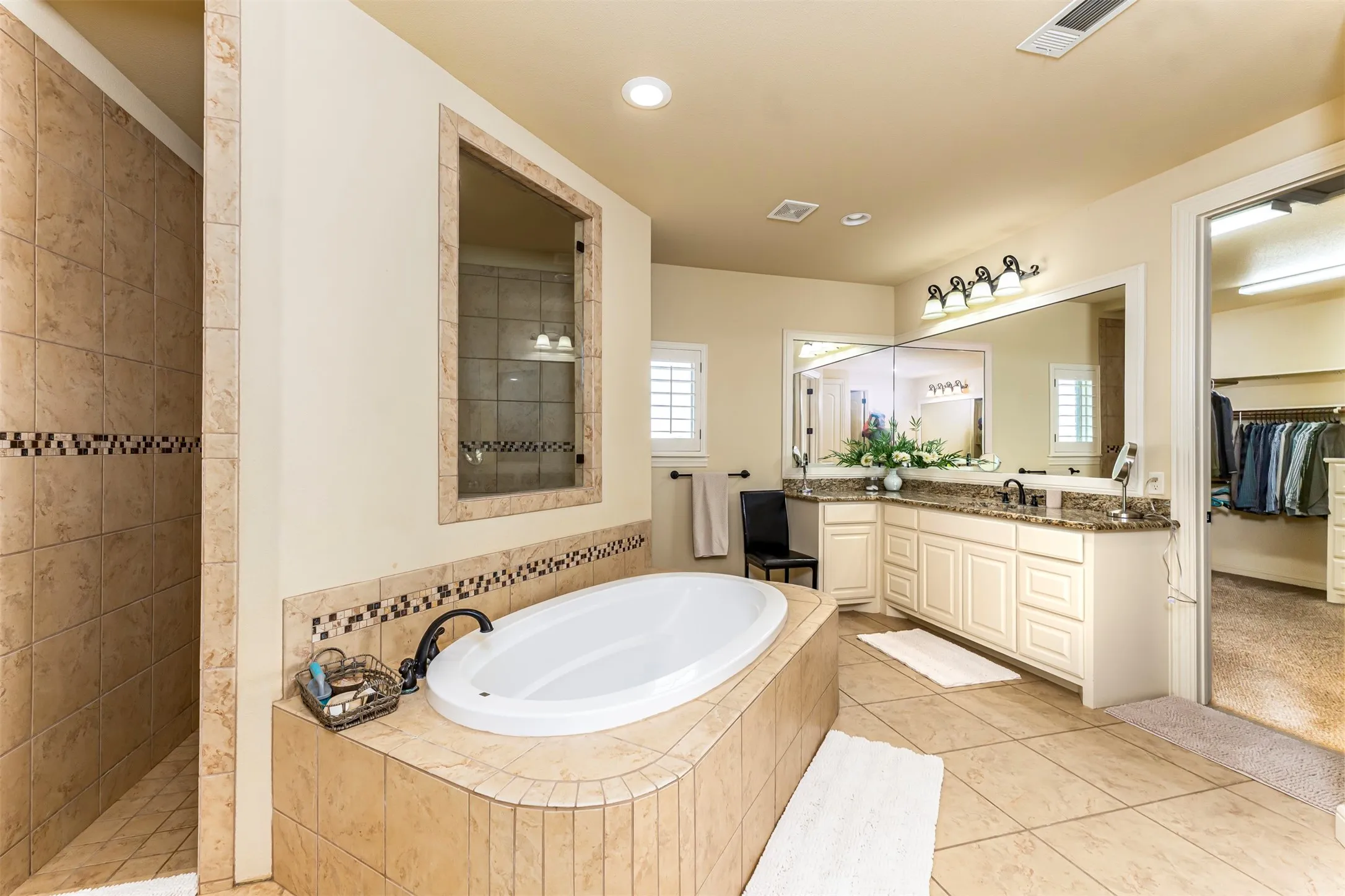 Tile flooring, built-in soaking tub, walk-in shower with tiled surround, dual vanity with undermount sinks, and a large wall-mounted mirror