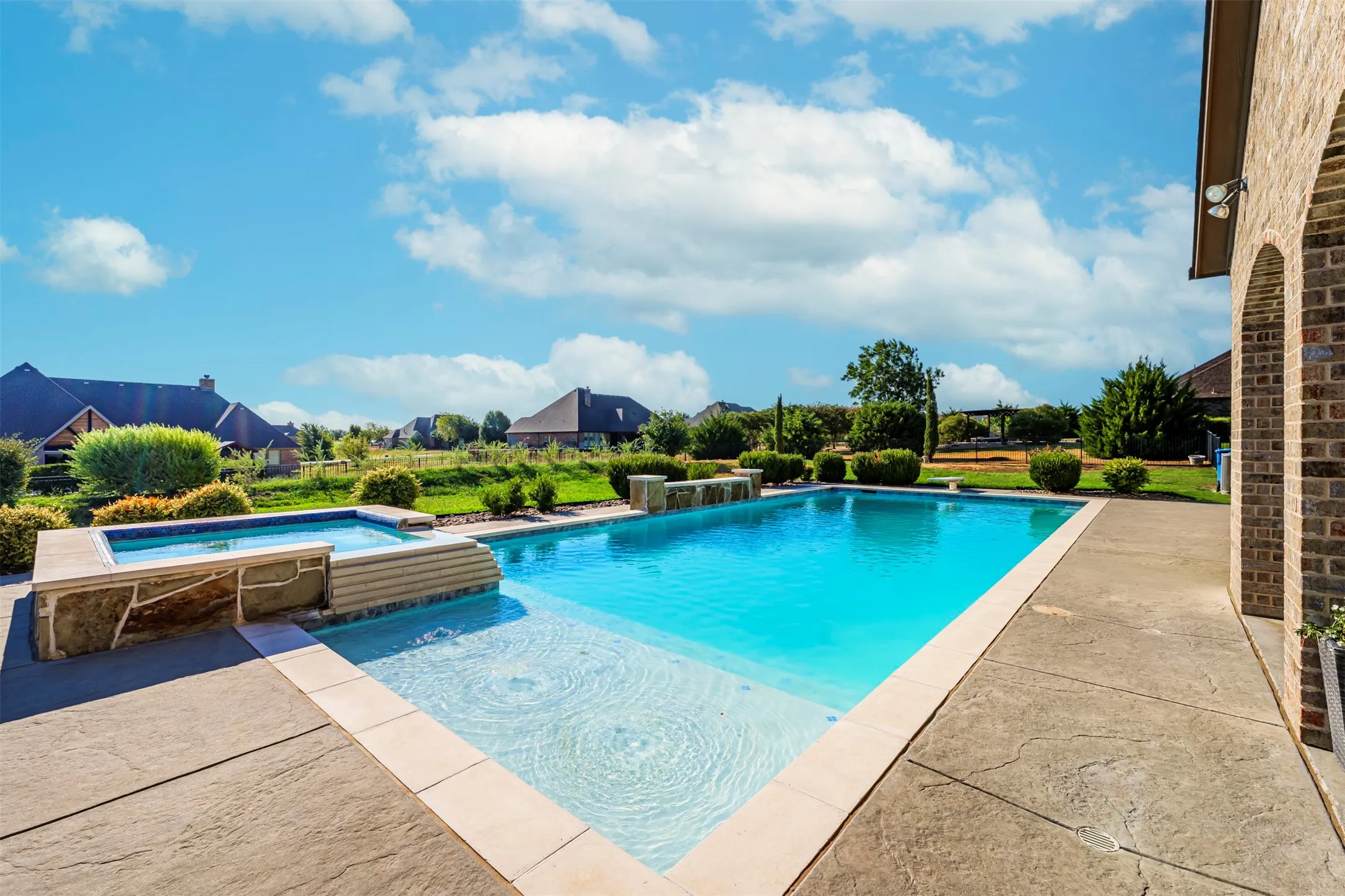 Expansive backyard featuring a swimming pool, integrated spa with stone accents, concrete patio, and manicured landscaping