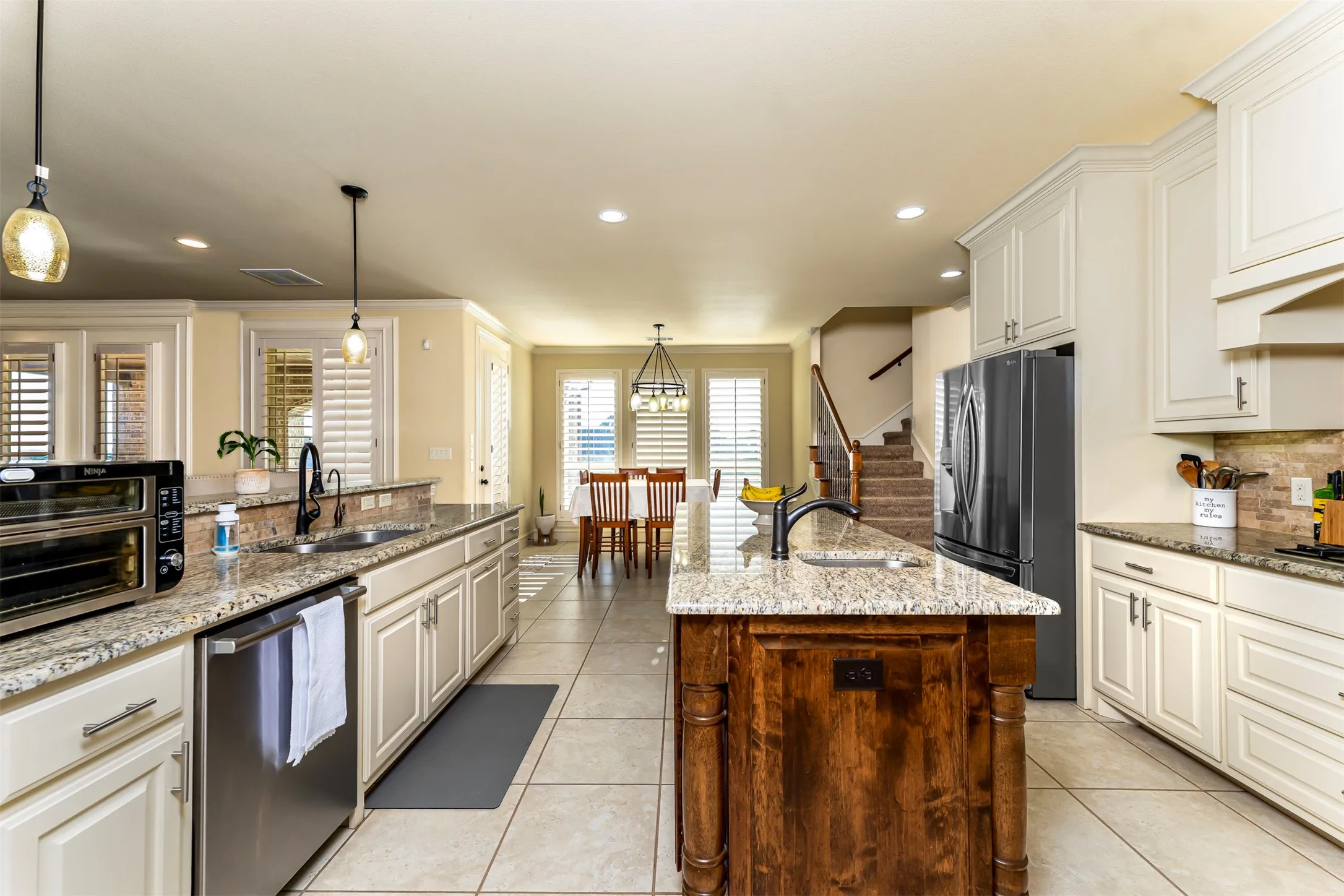 Spacious kitchen featuring light-toned cabinetry, granite countertops, a dark wood-finish island, stainless steel refrigerator, and tile flooring