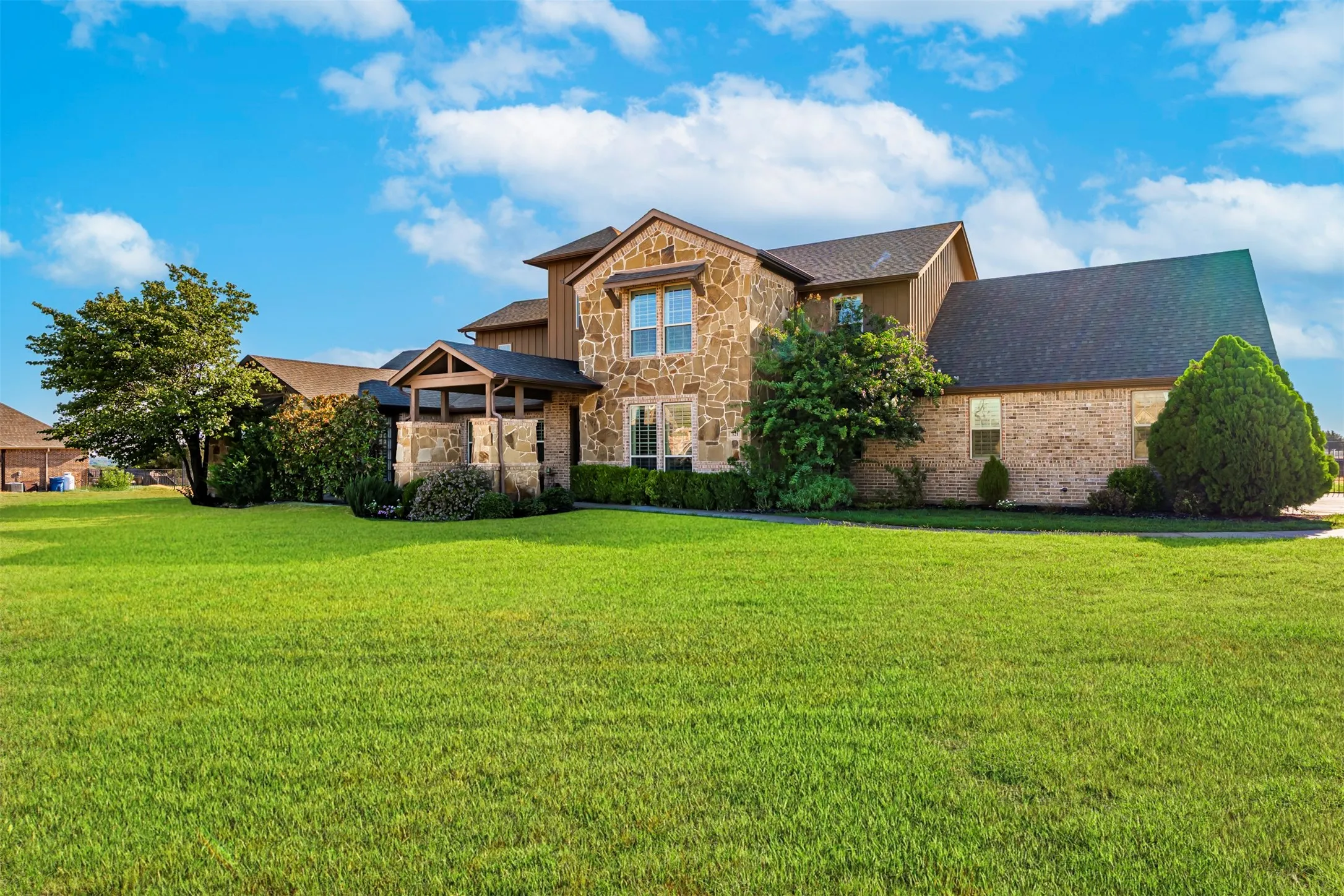 Stone and brick exterior with a covered entry, dark shingle roof, and mature landscaping