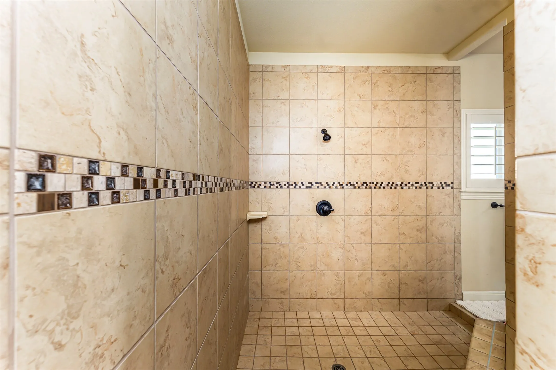 Walk-in shower with full-height tile surround, decorative mosaic tile accents, and dark bronze fixtures