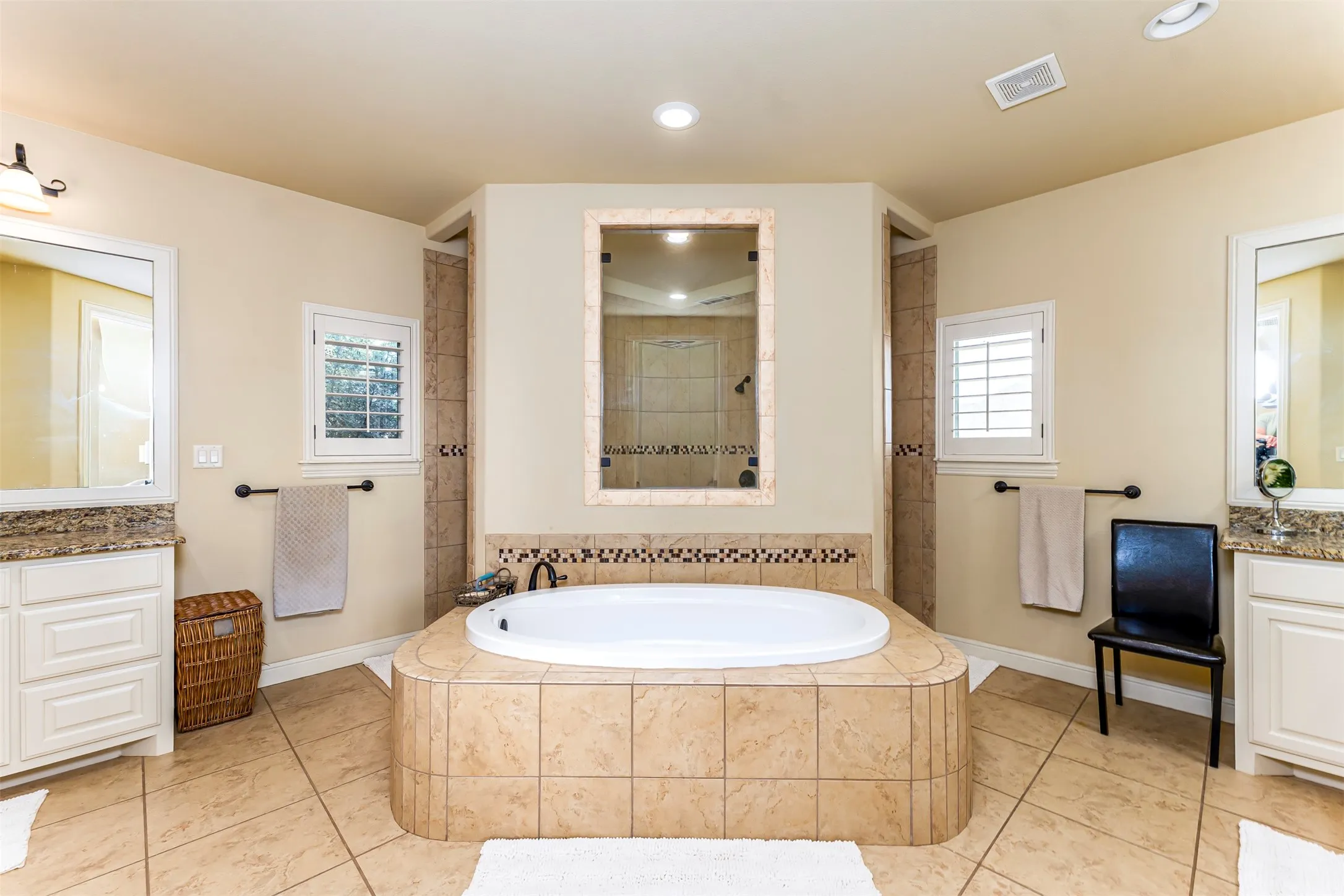 Built-in soaking tub with tile surround, dual vanity sinks with stone countertops, and tile flooring