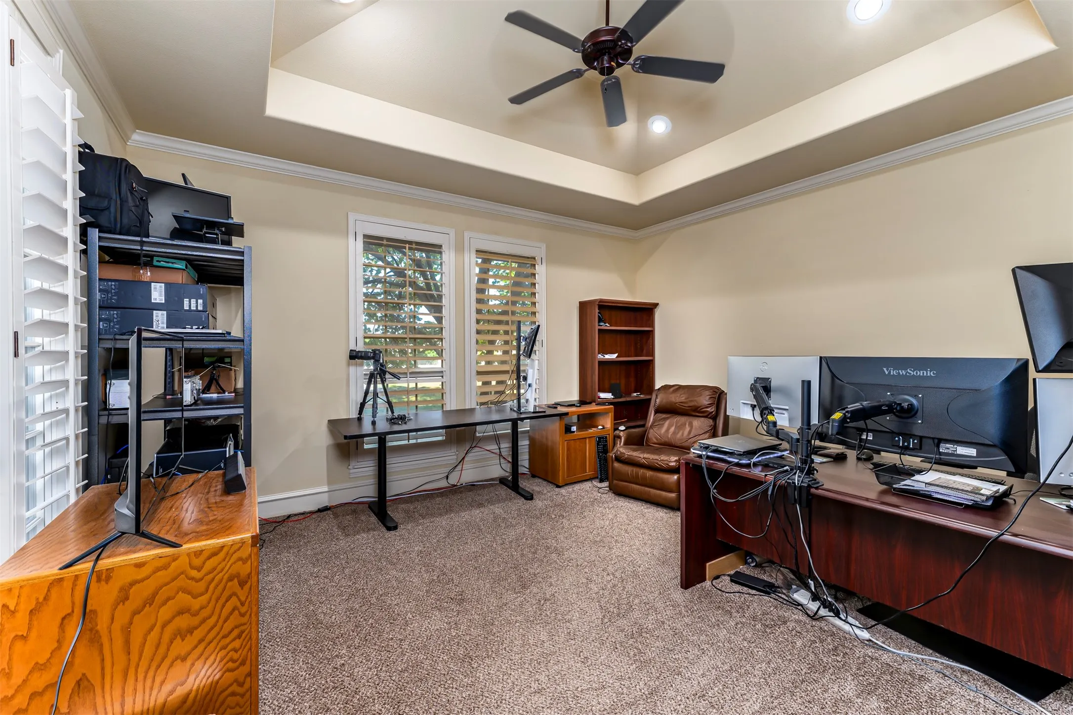 Tray ceiling with recessed lighting and a ceiling fan, plantation shutters, crown molding, and carpet flooring