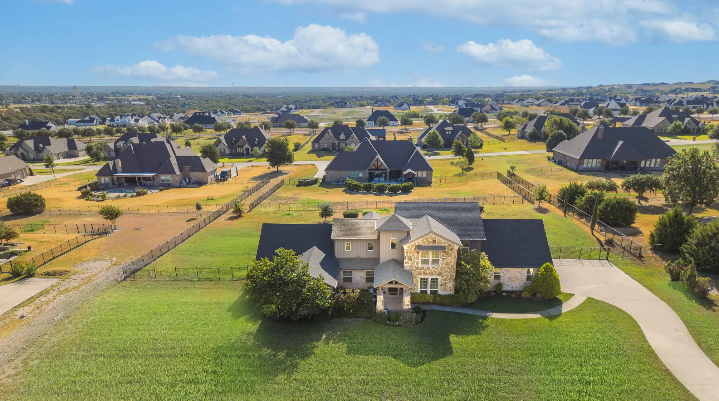Stone and siding exterior with a dark-pitched roof, an extended paved driveway, and a spacious front lawn