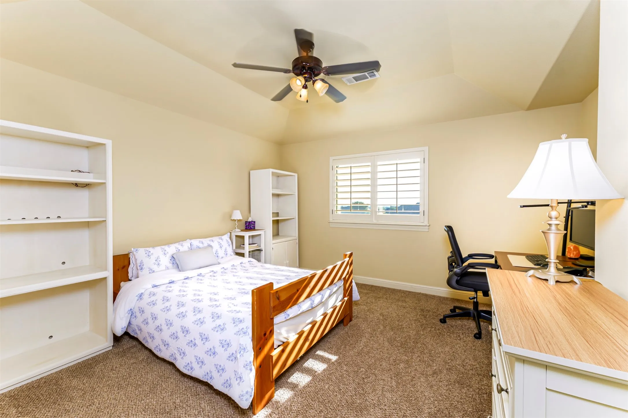 Carpeted room featuring a window with plantation shutters, a ceiling fan with integrated lighting, and a built-in bookshelf
