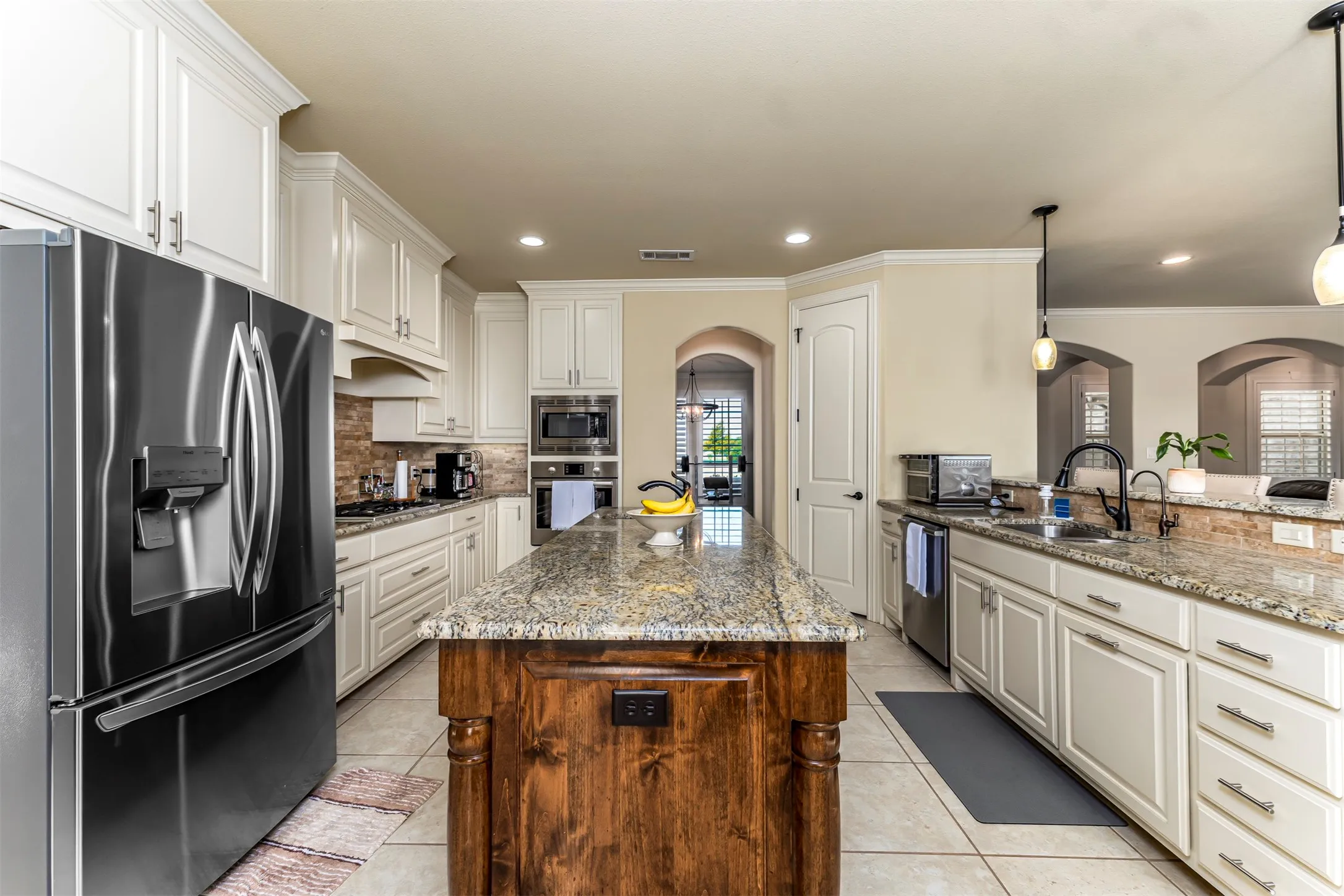 Kitchen featuring a large island with a stone countertop, white cabinetry, built-in stainless steel appliances, and tile flooring
