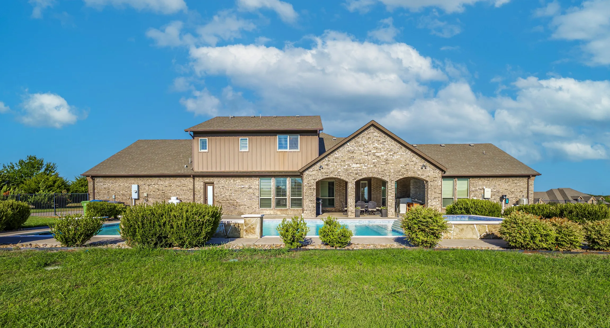 Brick exterior with a covered patio, multiple outdoor pools, and extensive lawn