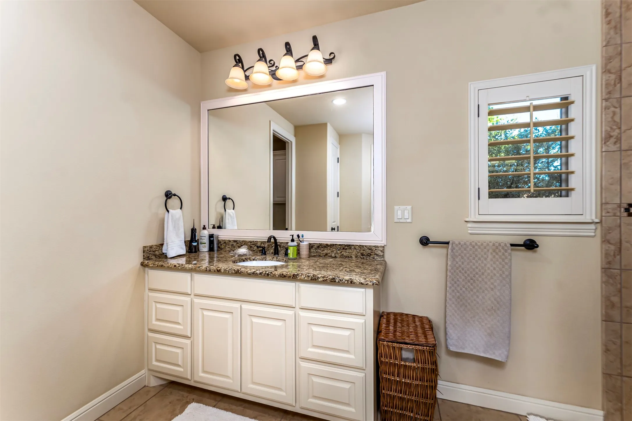 Spa-inspired primary bathroom vanity featuring a framed mirror with integrated lighting, granite countertop, and white cabinetry with multiple drawers and cabinet doors